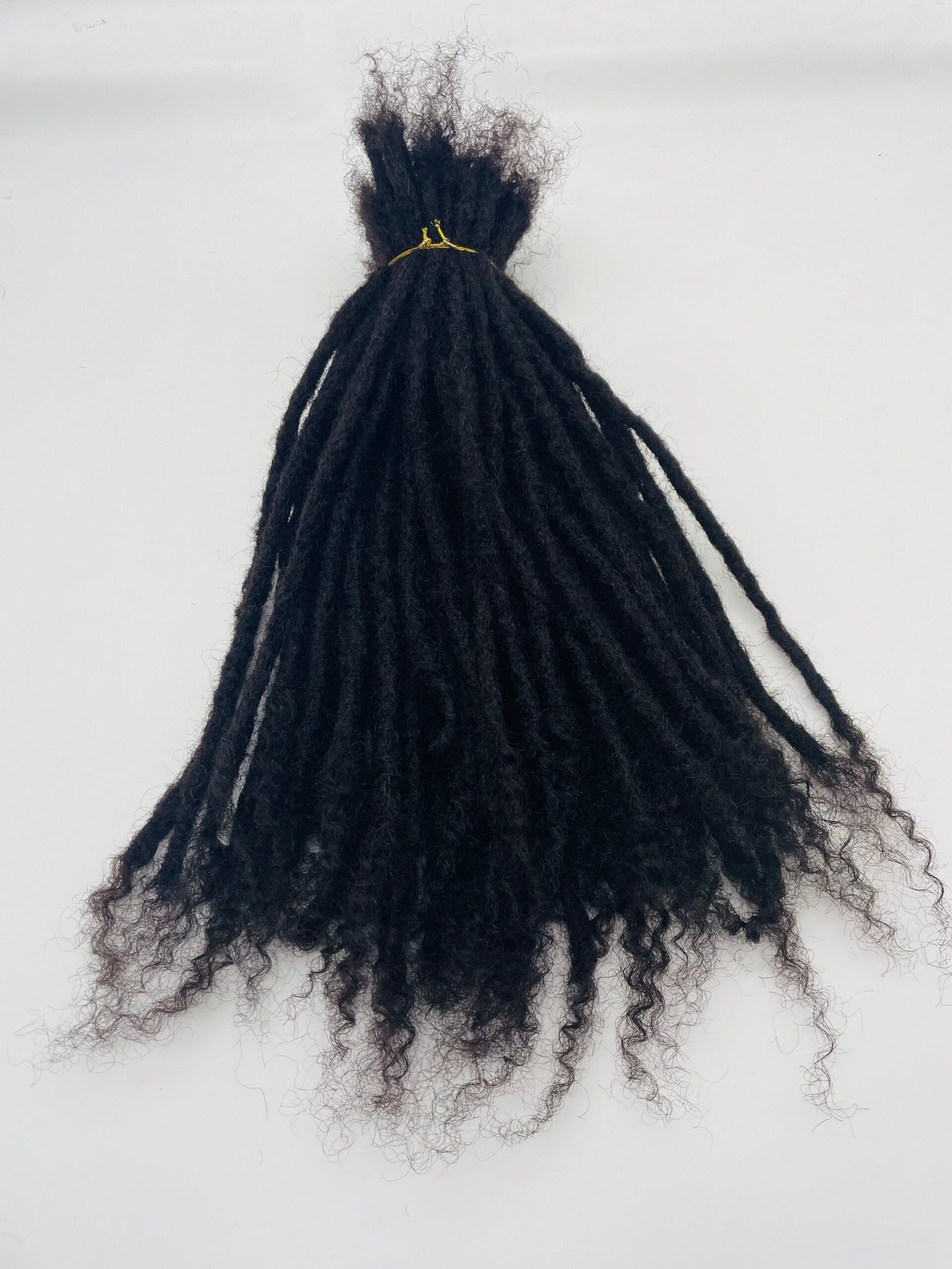 Back view of a person with long black dreadlocks gathered into a small top knot secured with a yellow hair tie on a light background.