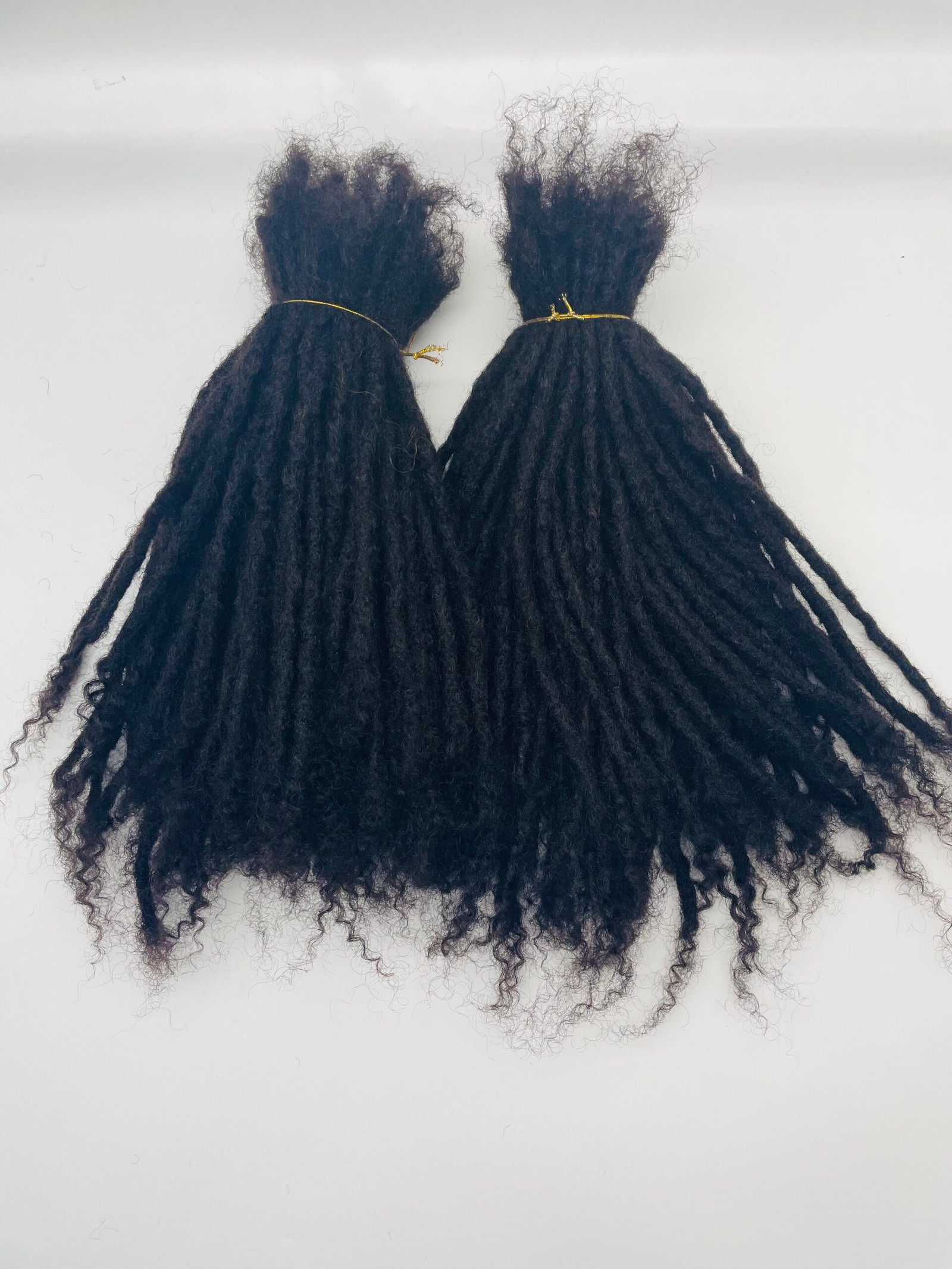 Two bundles of black dreadlocks tied with thin gold bands on a white surface.