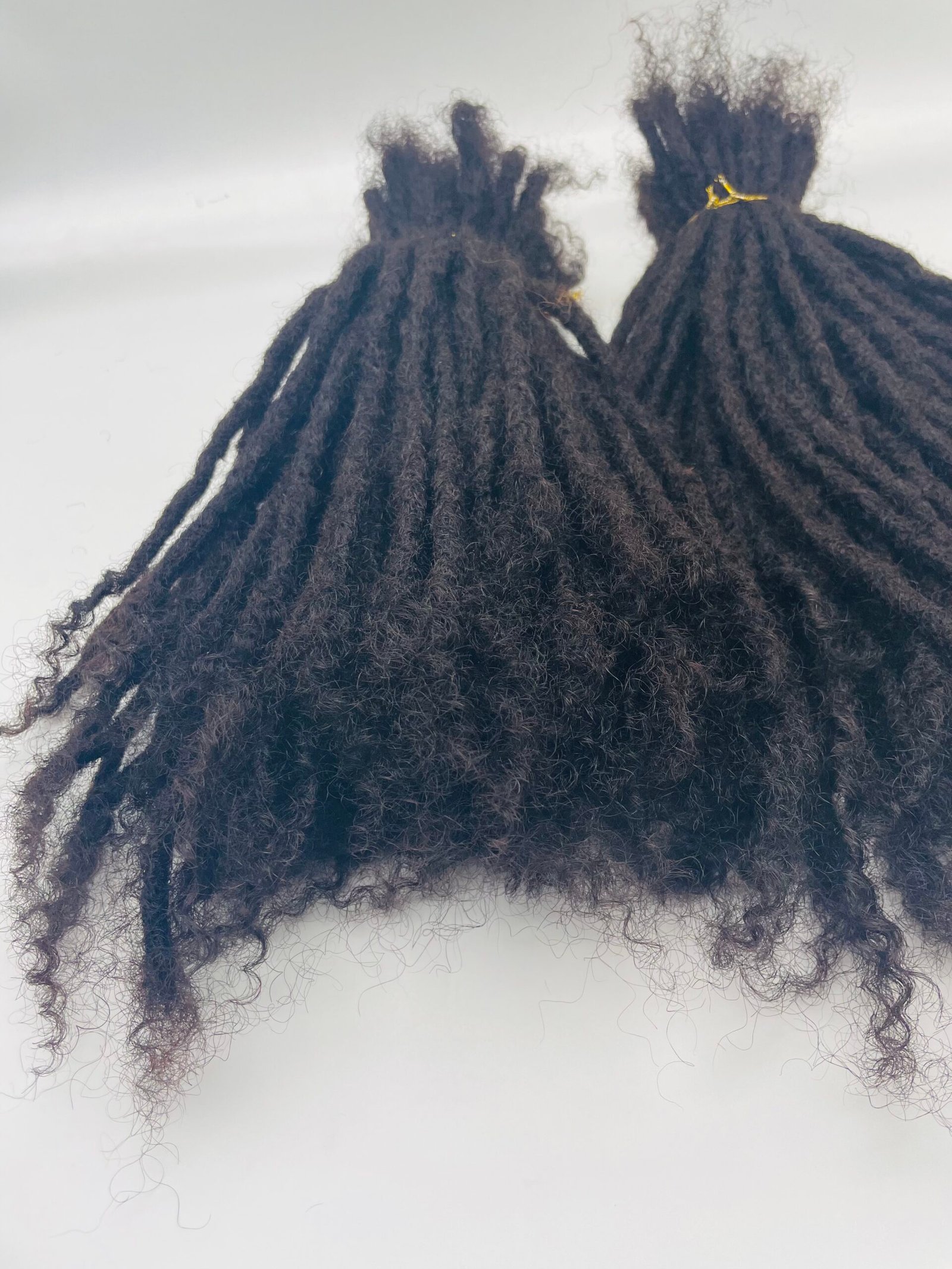 Two bundles of black dreadlocks tied at the top with small yellow bands, hanging against a pale background.