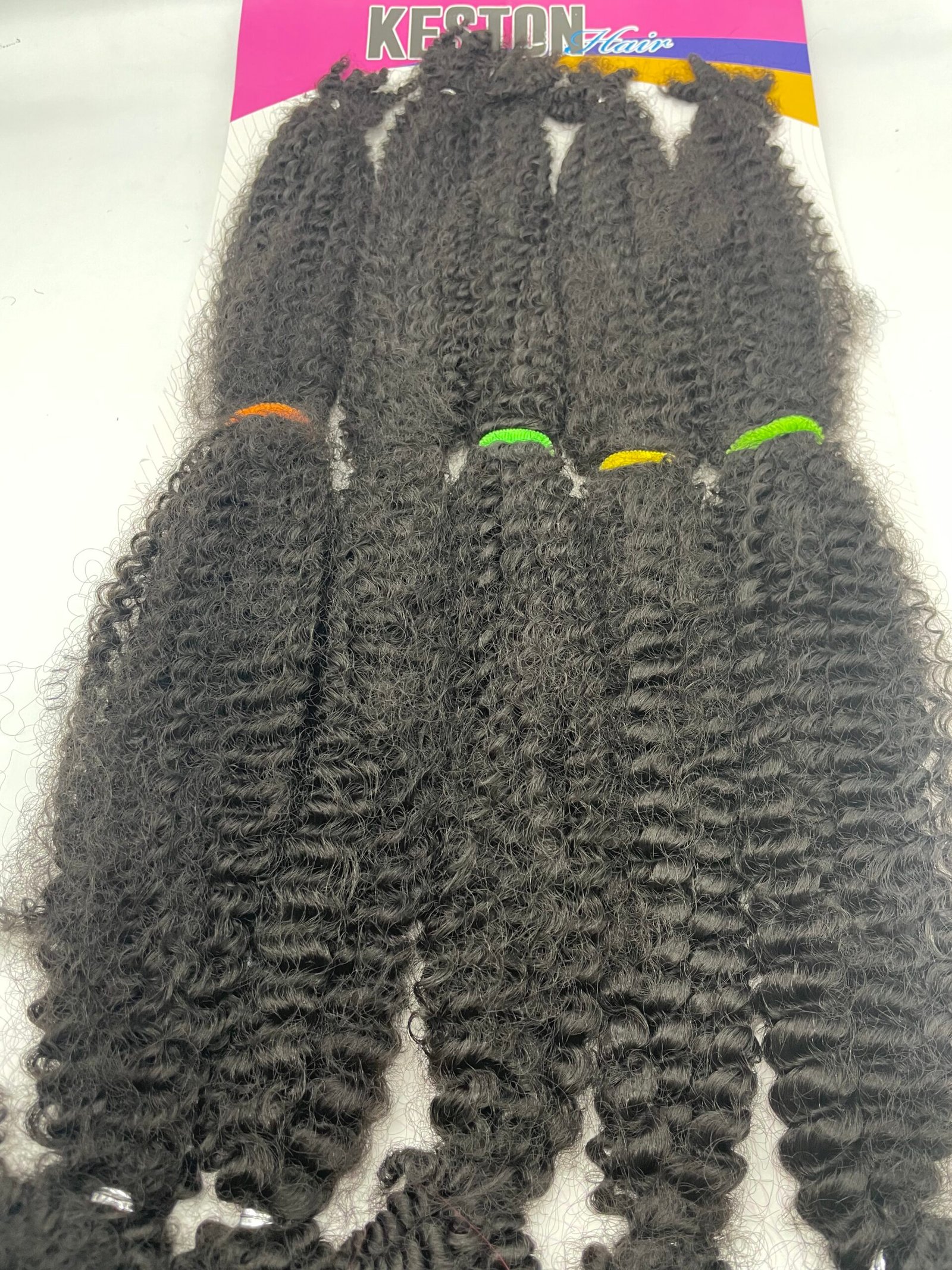 Bundles of black curly hair extensions with colored hair ties displayed on packaging (orange, green, yellow)