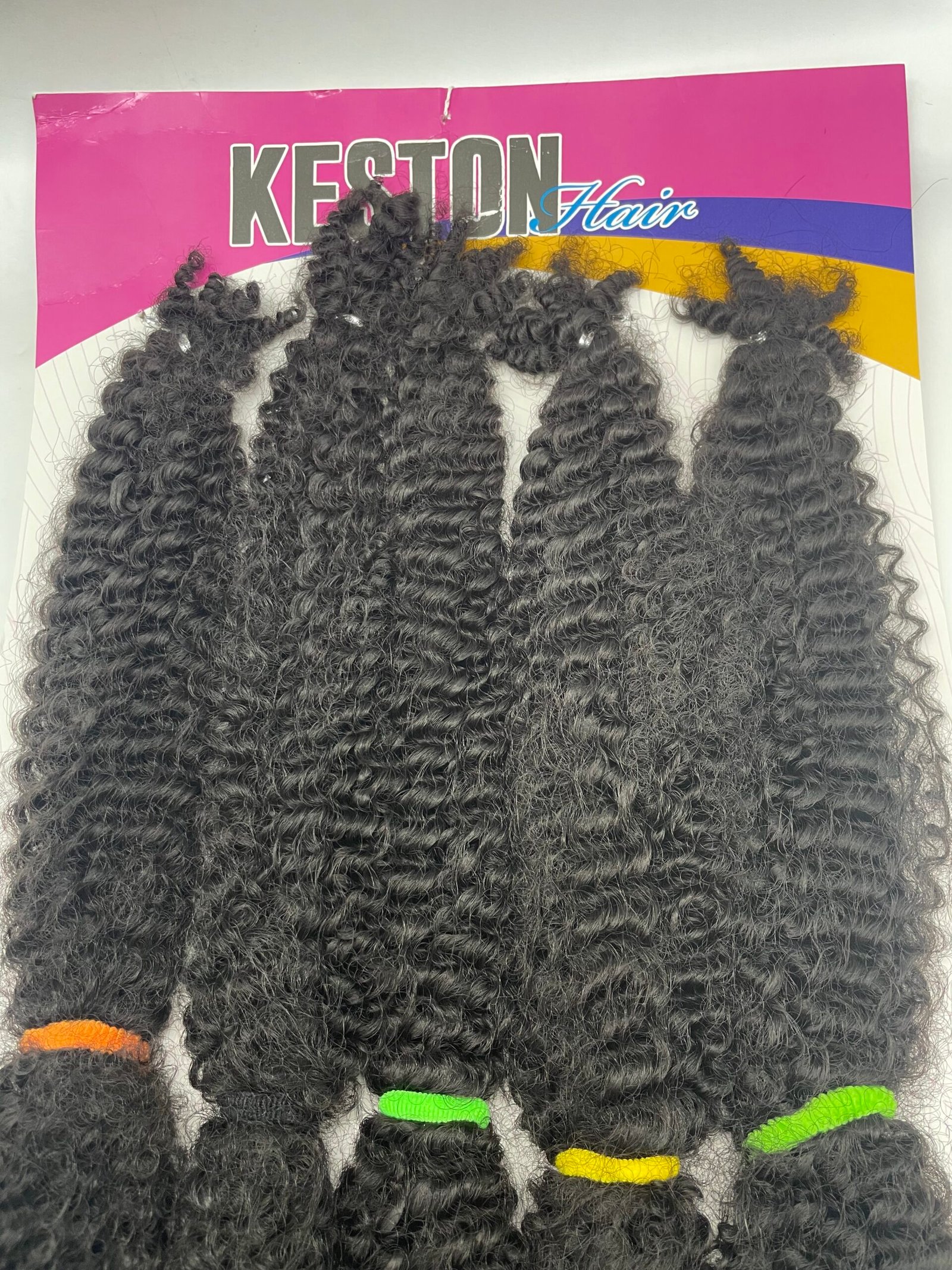Bundles of black curly hair extensions displayed on a pink Keston Hair packaging with purple and yellow stripes in the background.