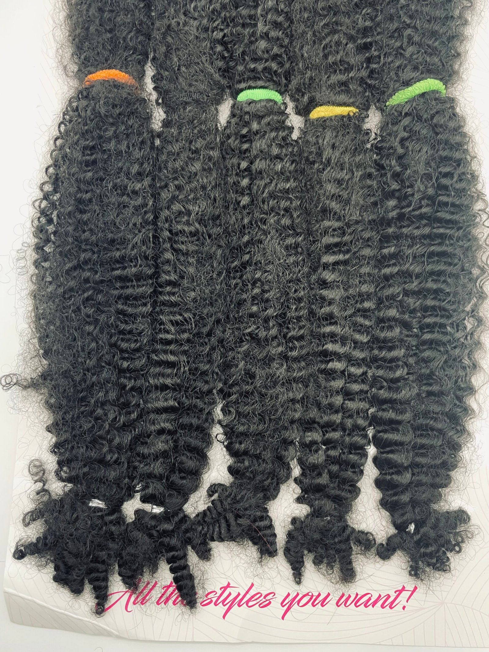 Bundles of long, tight-curly black hair extensions with colored bands (orange, green, yellow) on a white box backdrop.