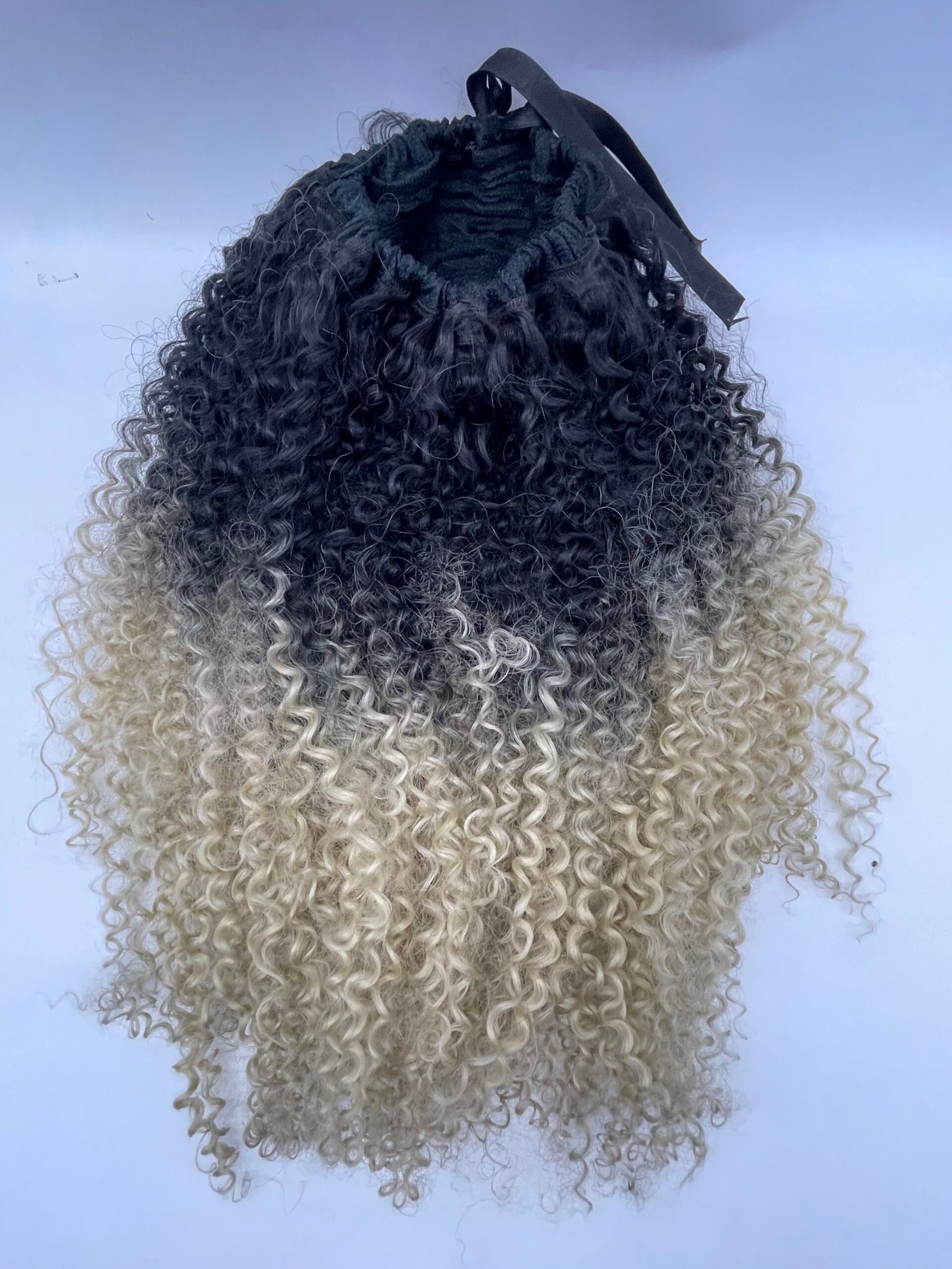 Back view of a person with tight dark-to-blonde ombre curls and a black hair band at the crown