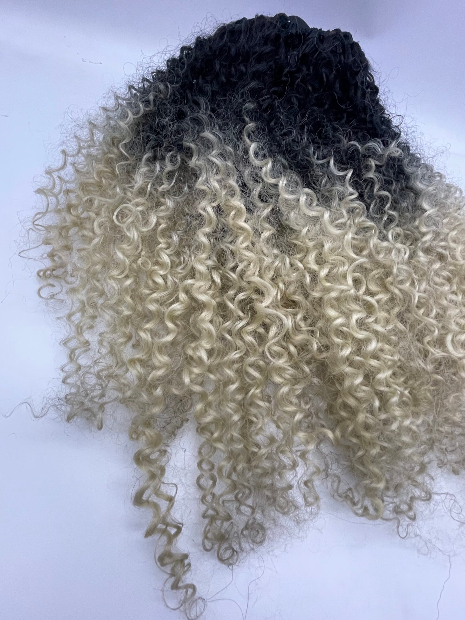 Back of a person’s head showing tight, two-tone curly hair: dark roots fading to pale blonde ends.