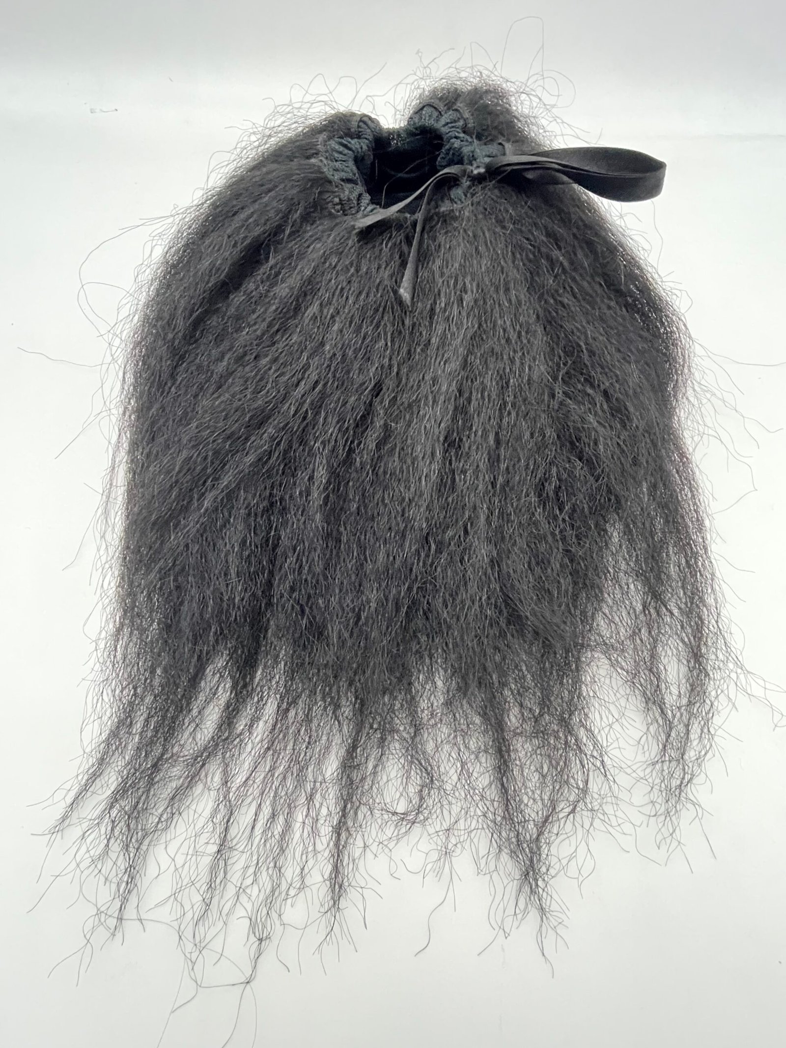 Dark, long, frizzy black hair pulled into a small ponytail tied with a black ribbon at the crown.