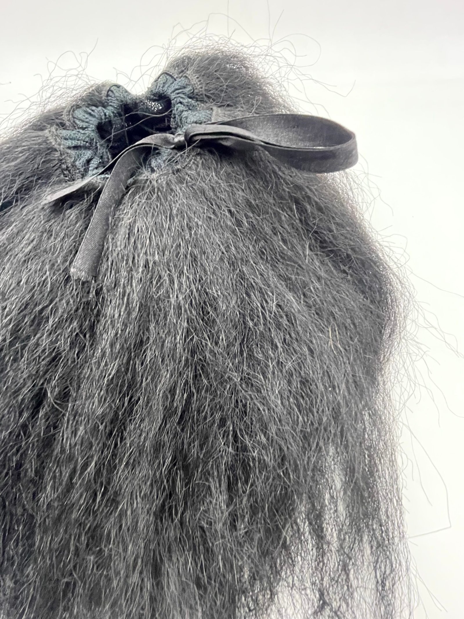 Close-up of dark, frizzy hair tied with a black ribbon and teal lace scrunchie at the back of the head