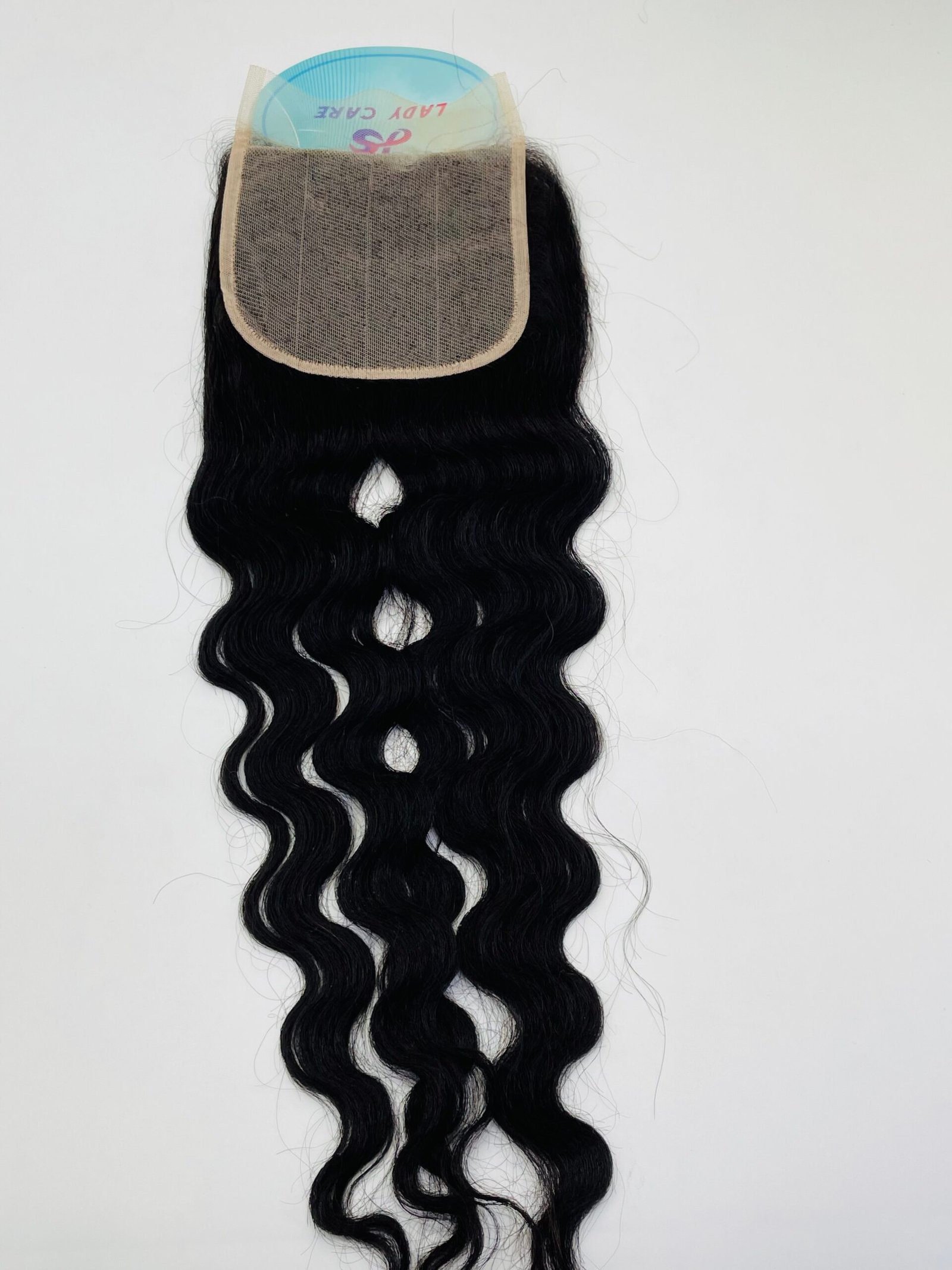 Wavy black hair weft with a beige lace cap showing the attachment base of a wig extension kit