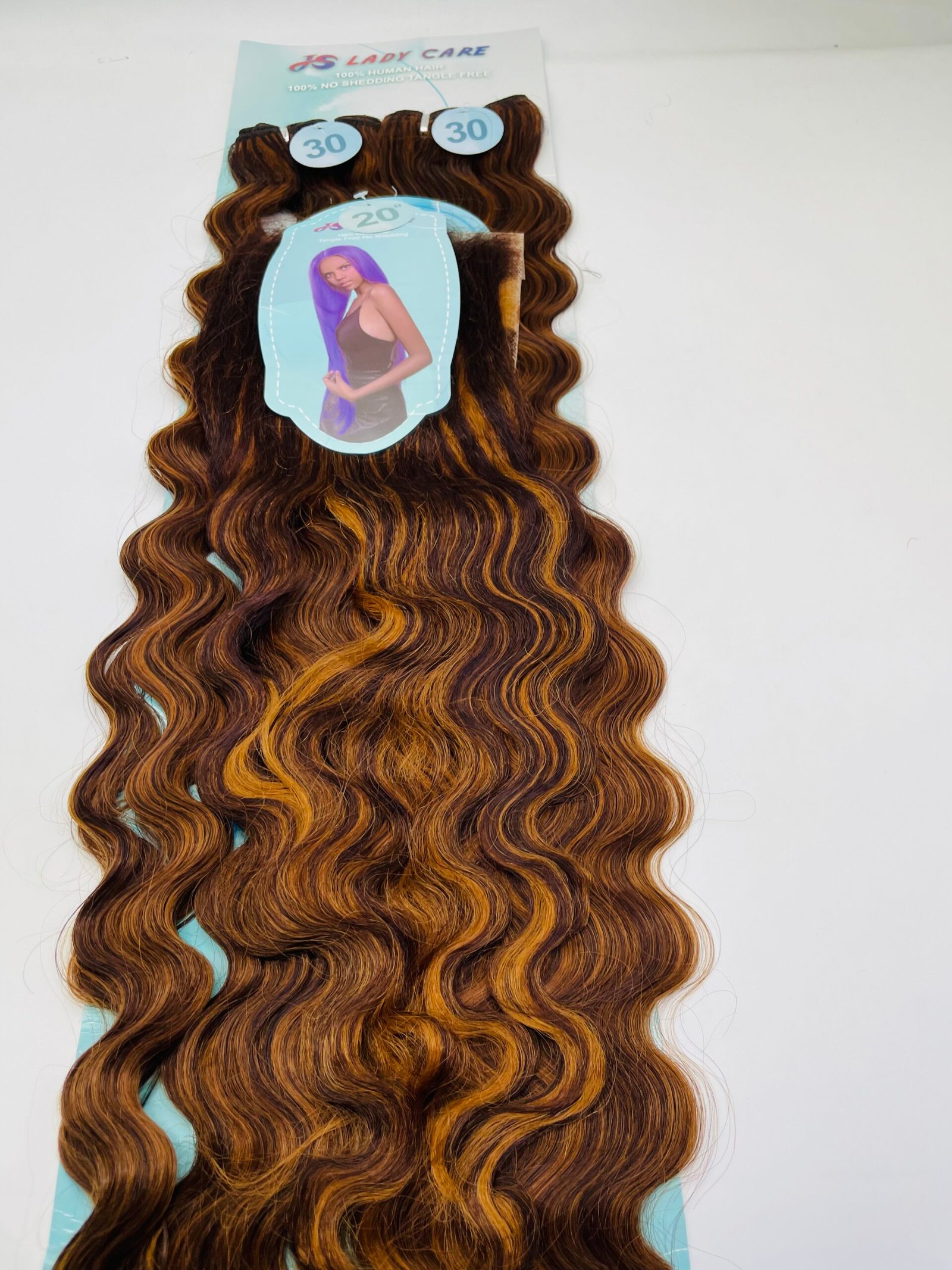Long wavy hair extensions with brown and orange highlights laid on a light blue display card