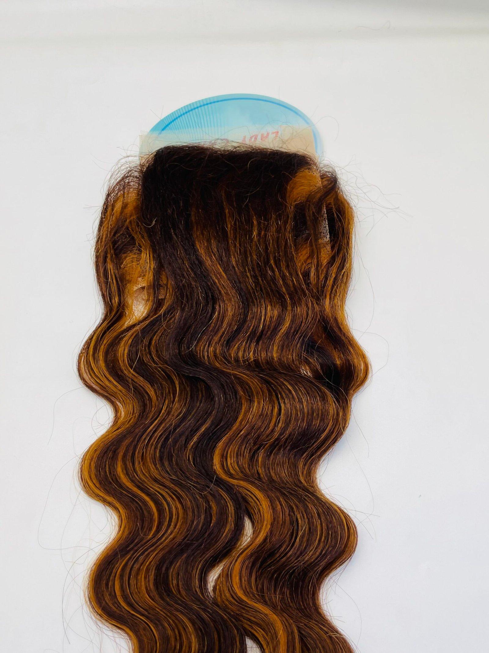 Back of head with long wavy brown hair and orange highlights, a blue rounded hairbrush resting on the scalp area