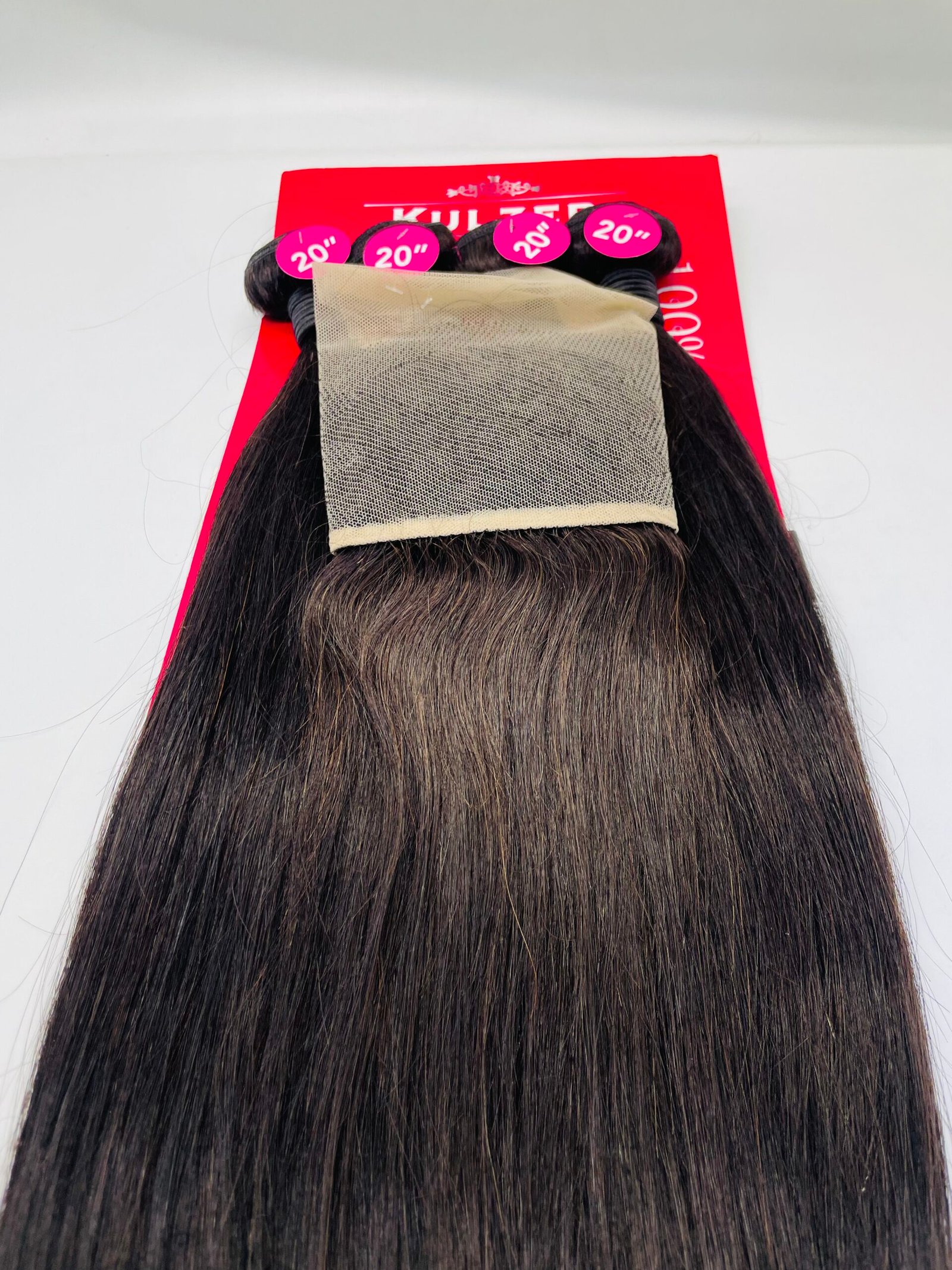 Dark brown hair extensions laid over a bright red display with pink 20" labels indicating length (20 inches).