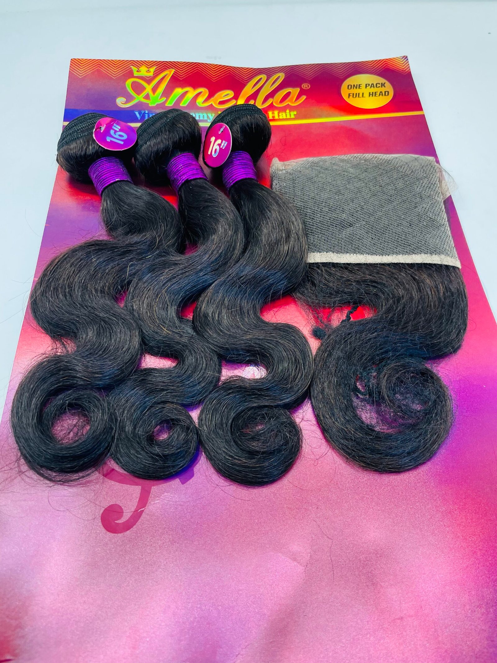 Three black wavy hair extension bundles with purple bands on a bright pink Amella display card with a mesh wrap nearby.