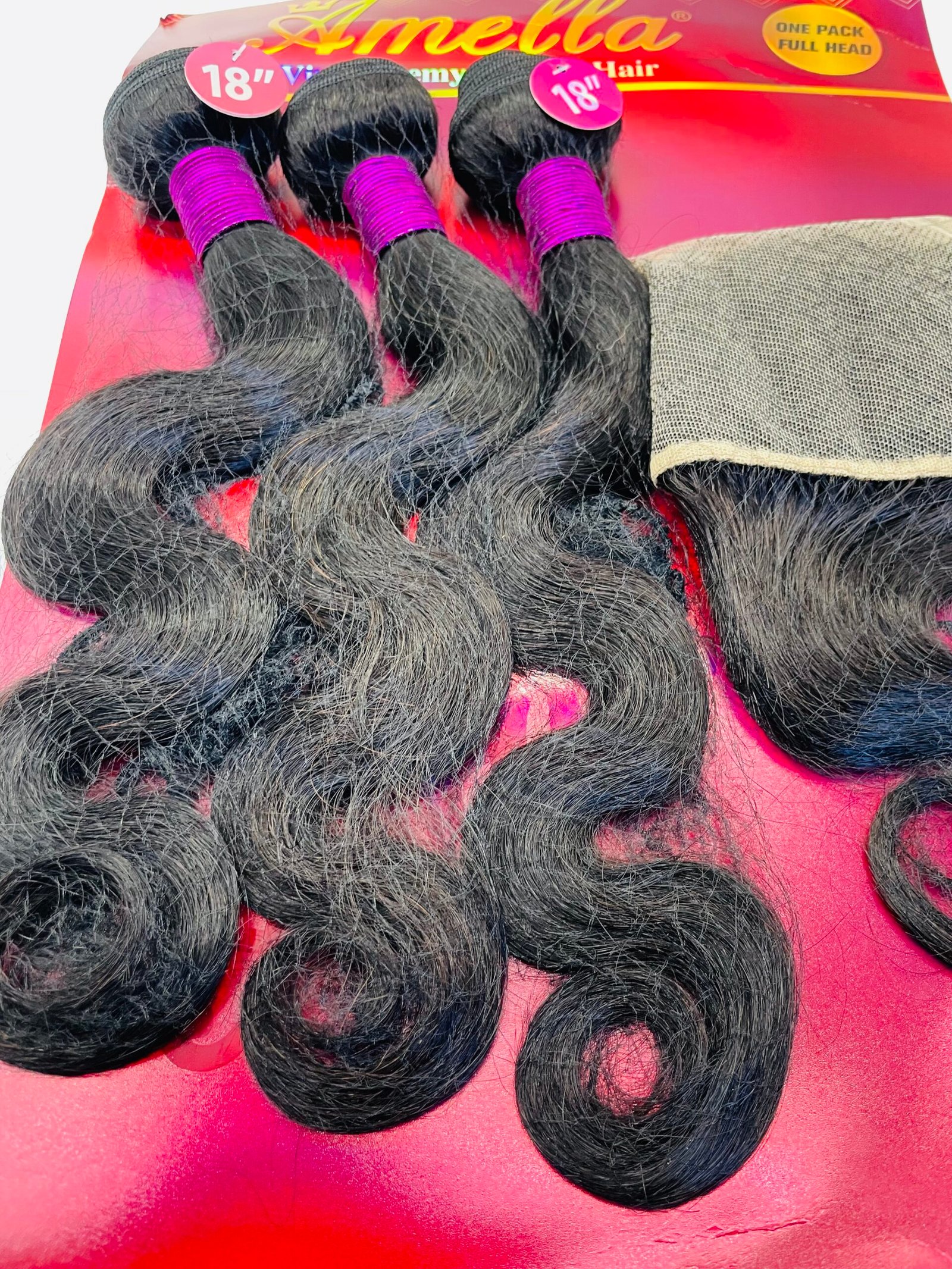 Bundles of long black hair extensions tied with bright pink bands, laid on a red display background showing 18" length