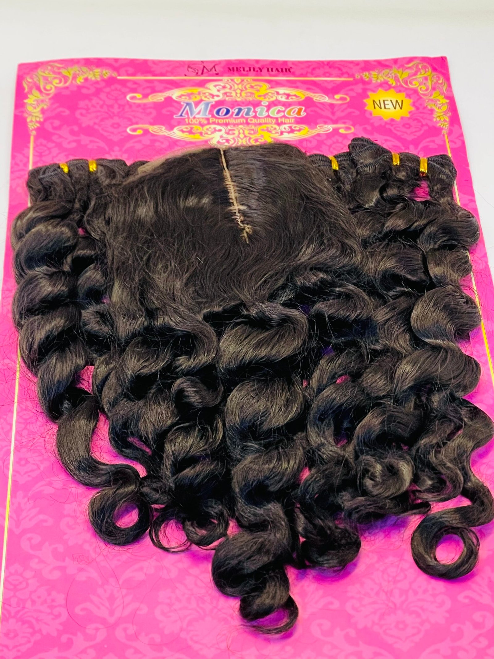 Bundles of dark curly hair extensions laid on a bright pink card with gold decorative patterns, featuring the word 'Monica' and a yellow 'NEW' badge in the top right corner.