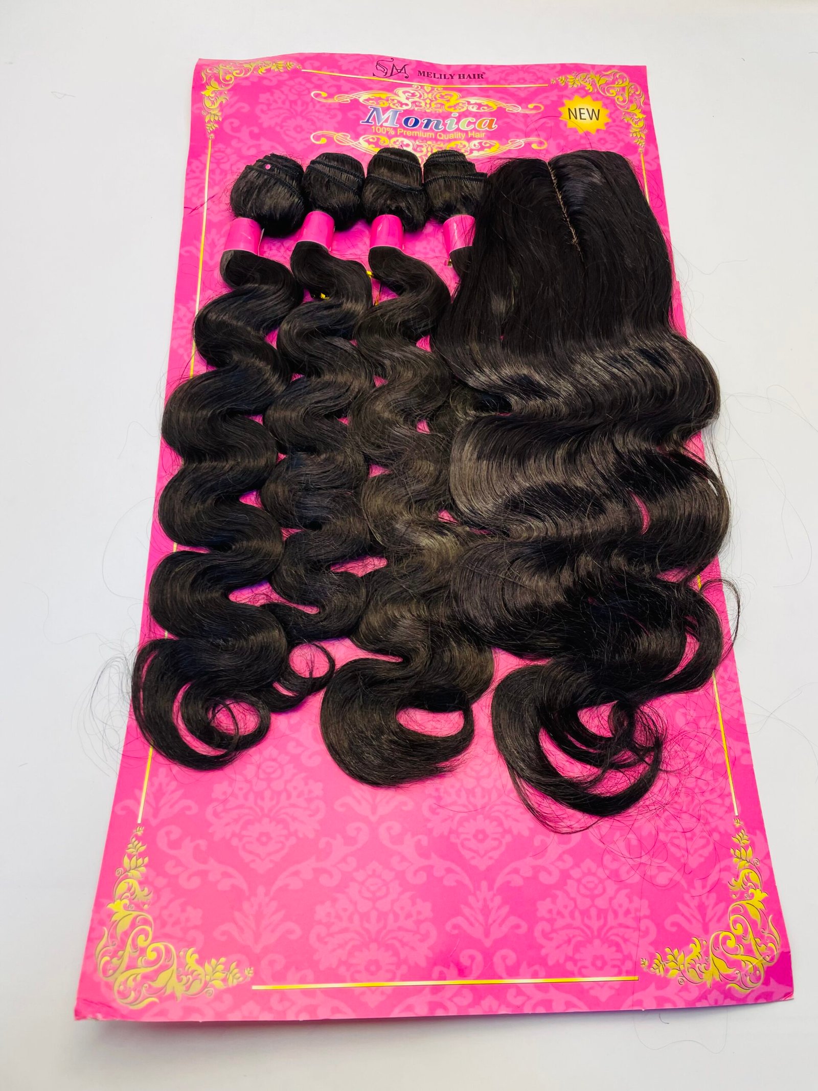 Set of long black wavy hair extensions laid on a bright pink display card with gold decorative pattern.
