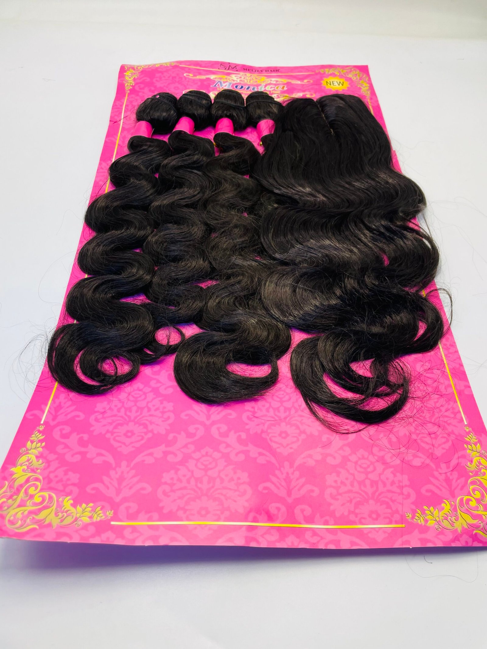 Bundles of long, dark wavy hair extensions laid on a bright pink decorative packaging.