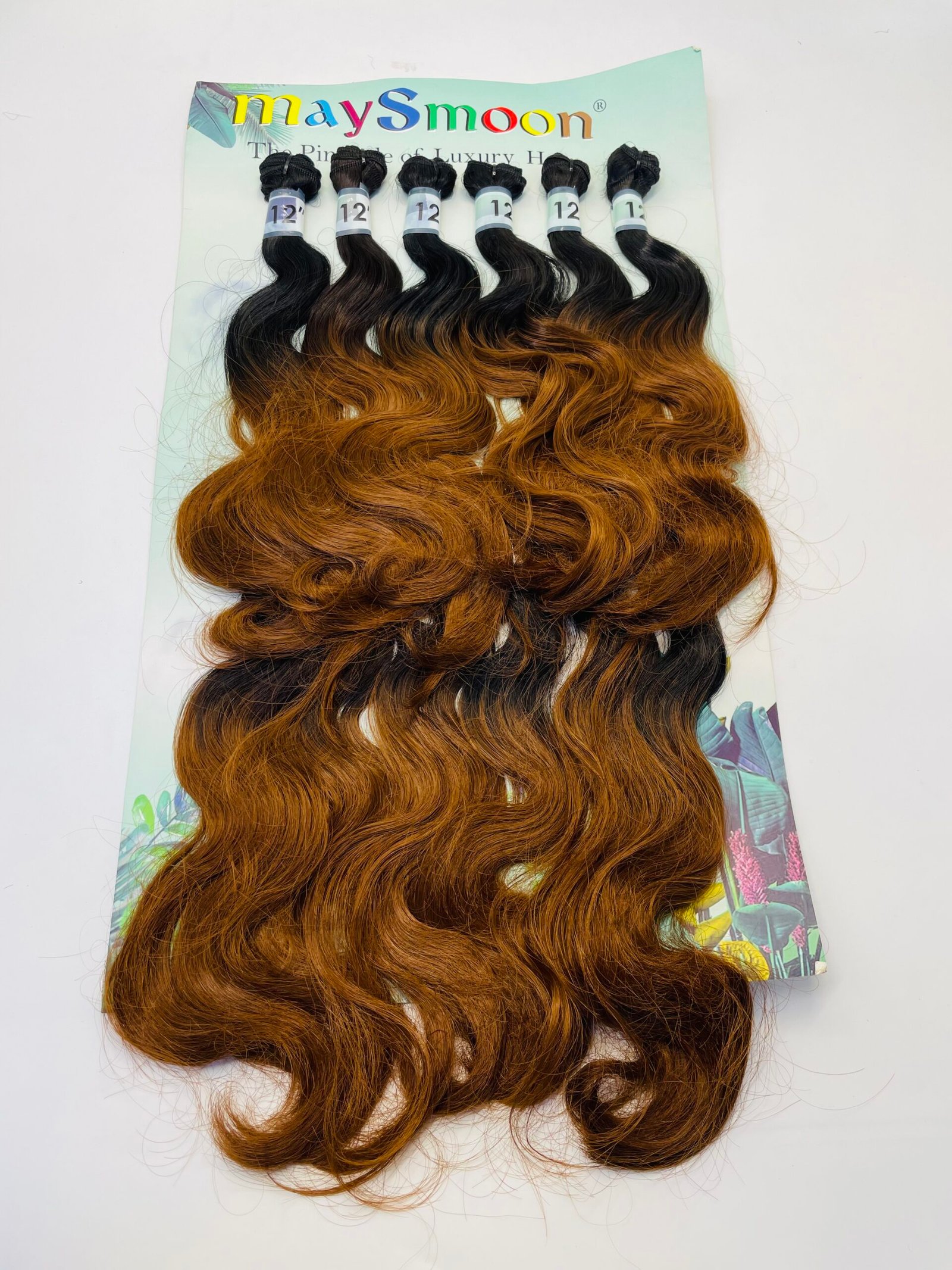 Six bundles of wavy ombre hair extensions, black roots fading to copper brown, displayed on a pastel green card.