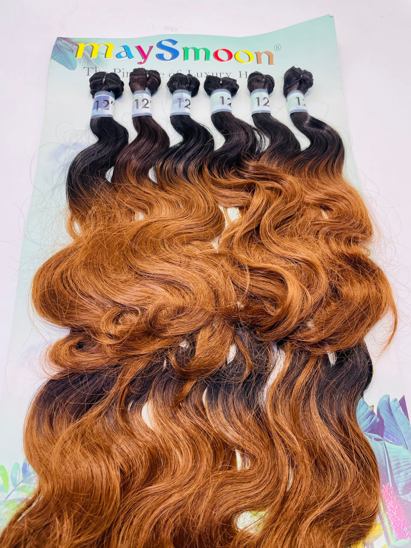 Six ombre hair extension wefts from black to copper, arranged on a pale display card with blue 12" bands on each bundle.