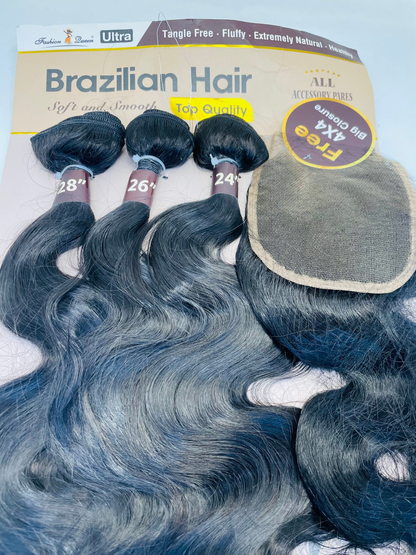 Assorted long black hair bundles labeled 28", 26", and 24" resting on a cardboard box with a fabric wig cap nearby.