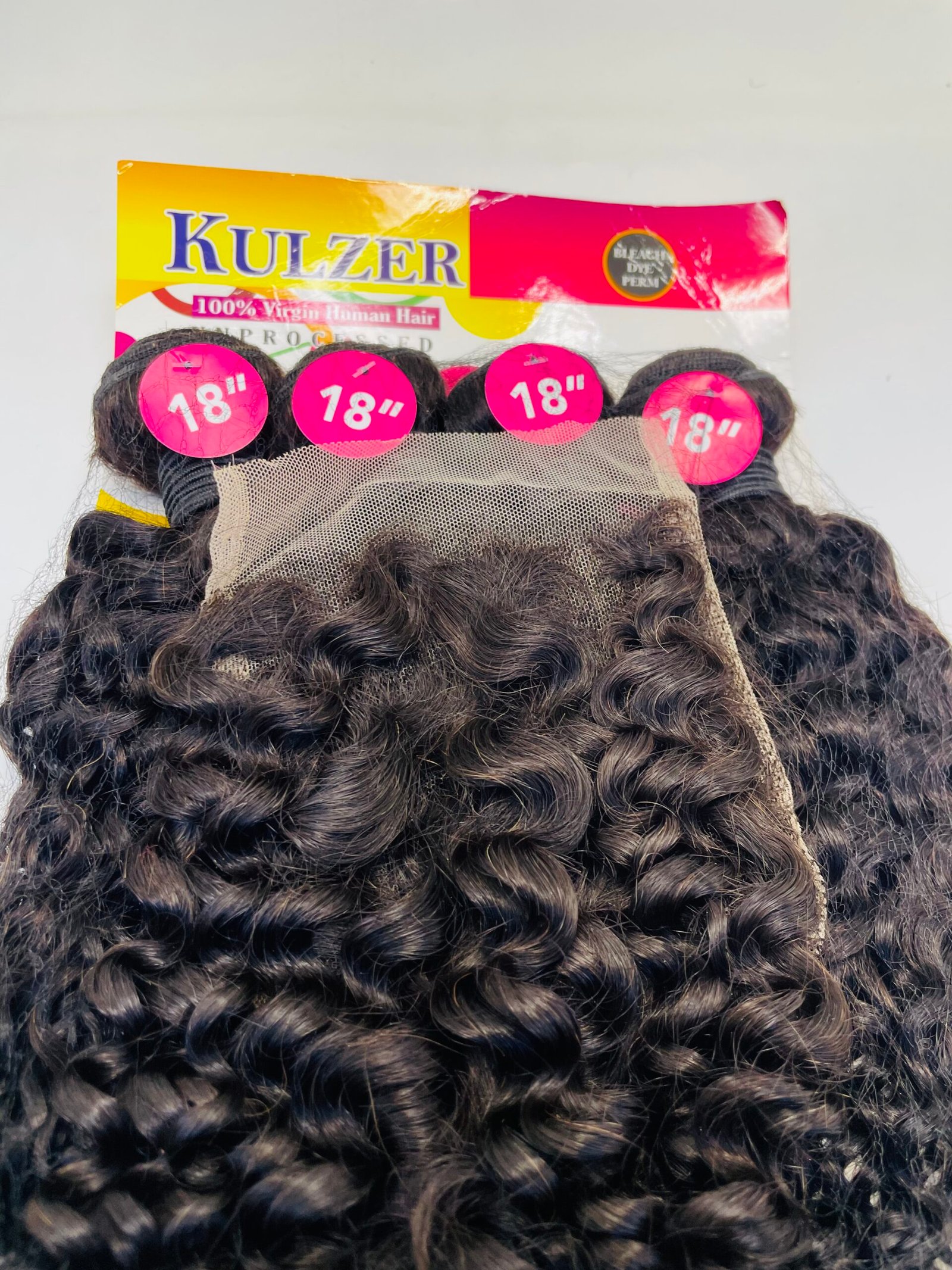 Dark brown curly wig with 18-inch length pink labels and lace netting visible, displayed on a colorful box in the background.