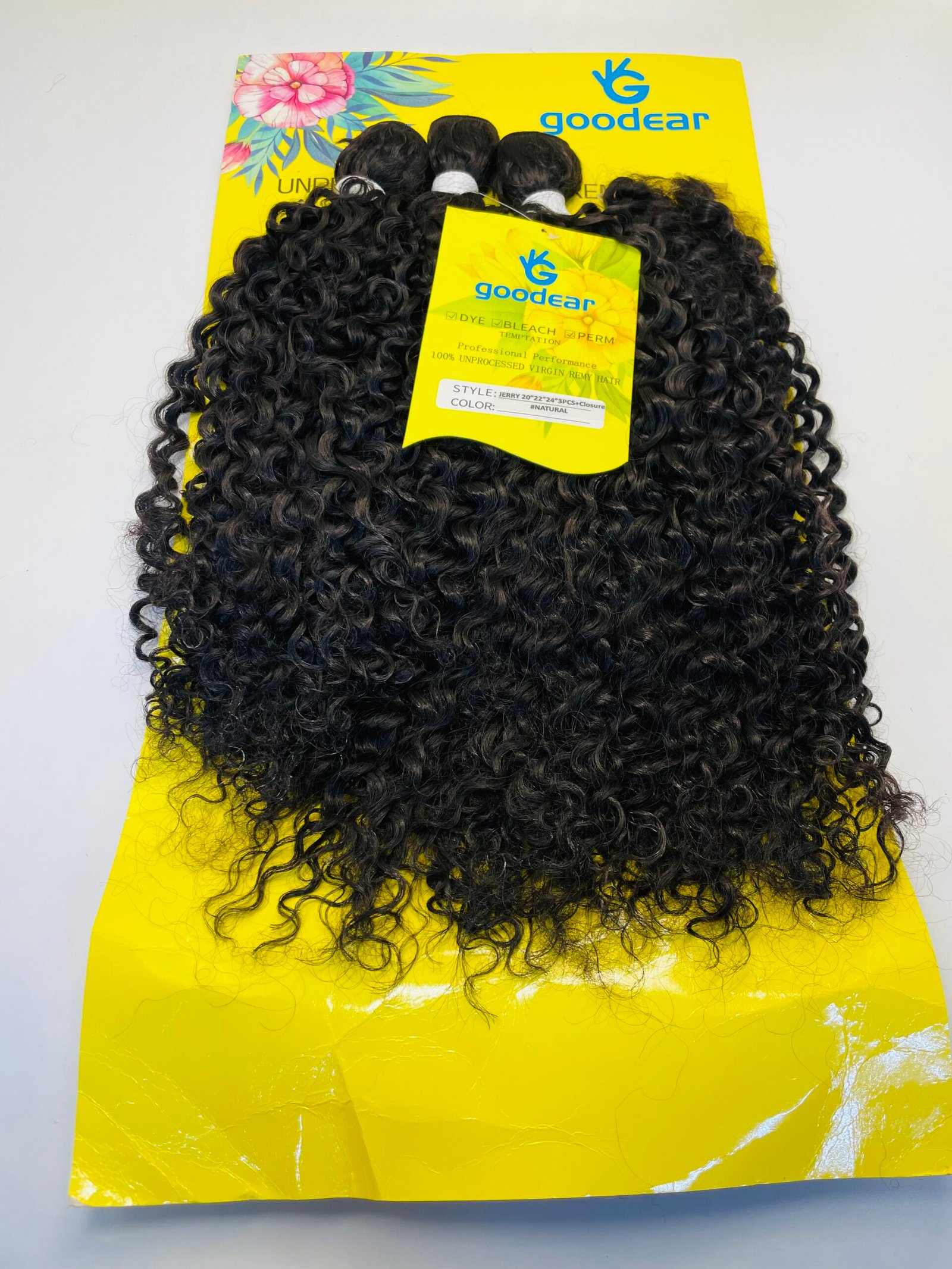 Bundle of tight, curly black hair extensions laid over a bright yellow Goodear packaging card.