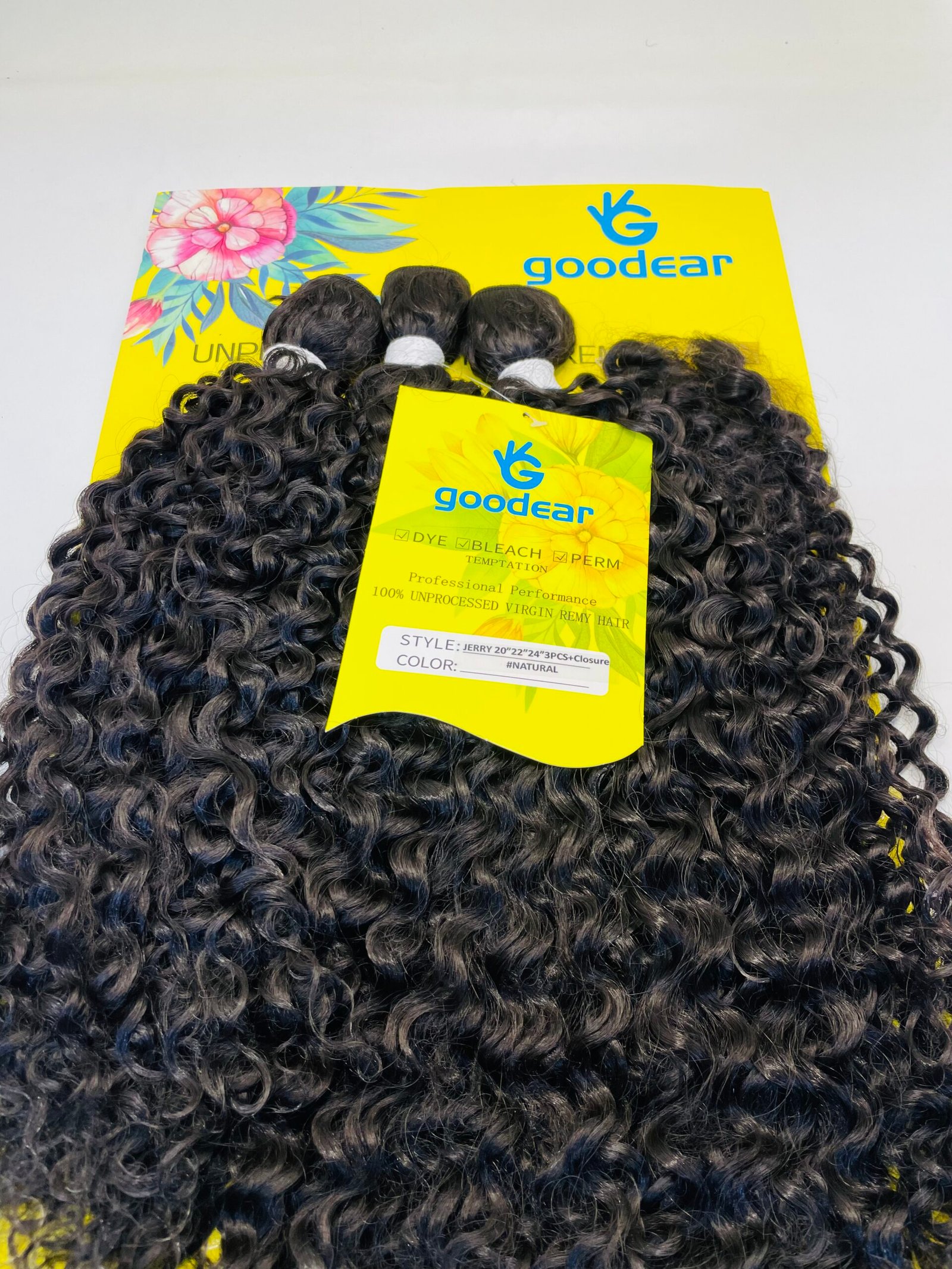 Bright yellow Goodear hair product box with a tropical flower design and bunches of tight black curly hair extensions spilling over it