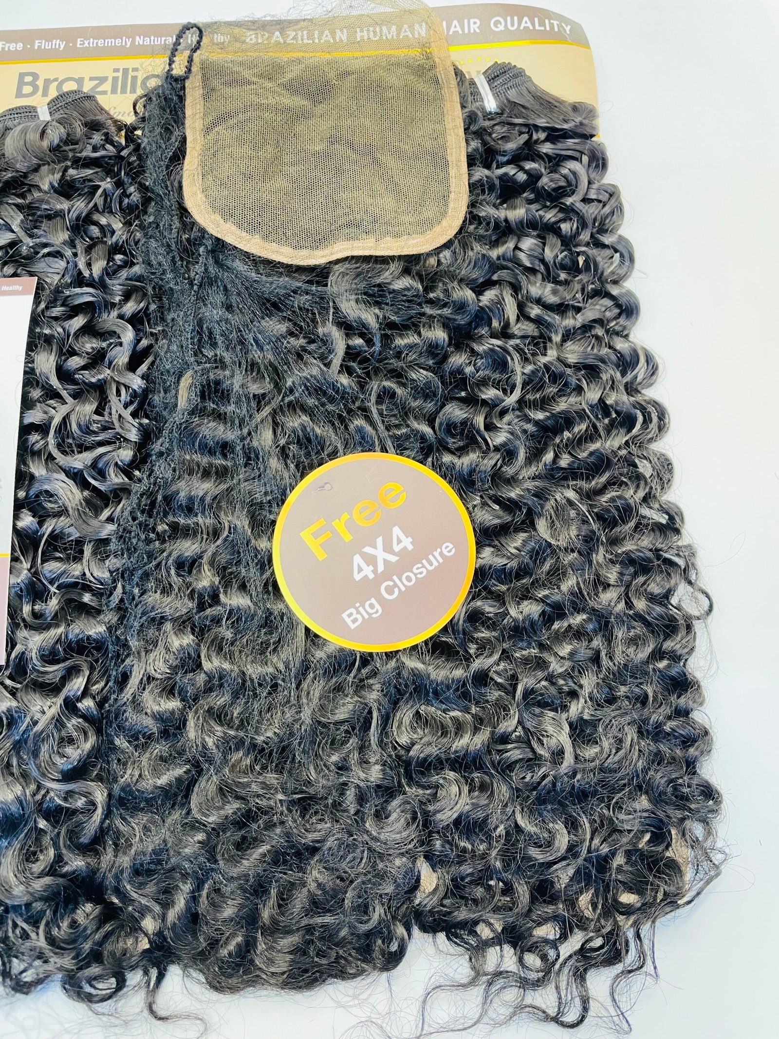Curly black hair extension bundle with a beige lace closure cap and a yellow-tag sticker reading 'Free 4x4 Closure' on top of the display card.