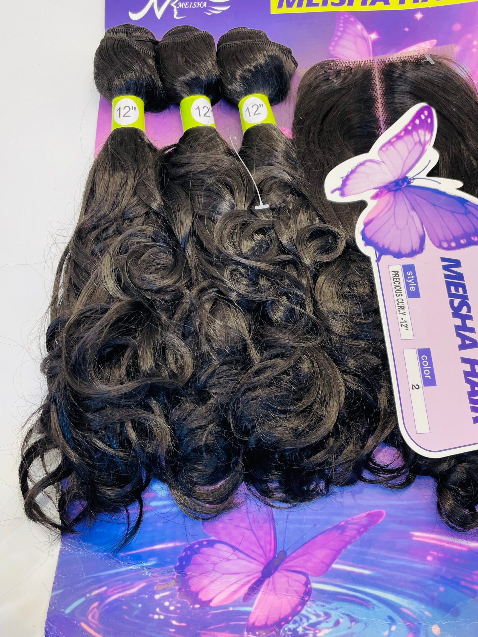 Bundles of dark brown curly hair with 12" labels on lime bands, arranged on a purple butterfly-themed backdrop