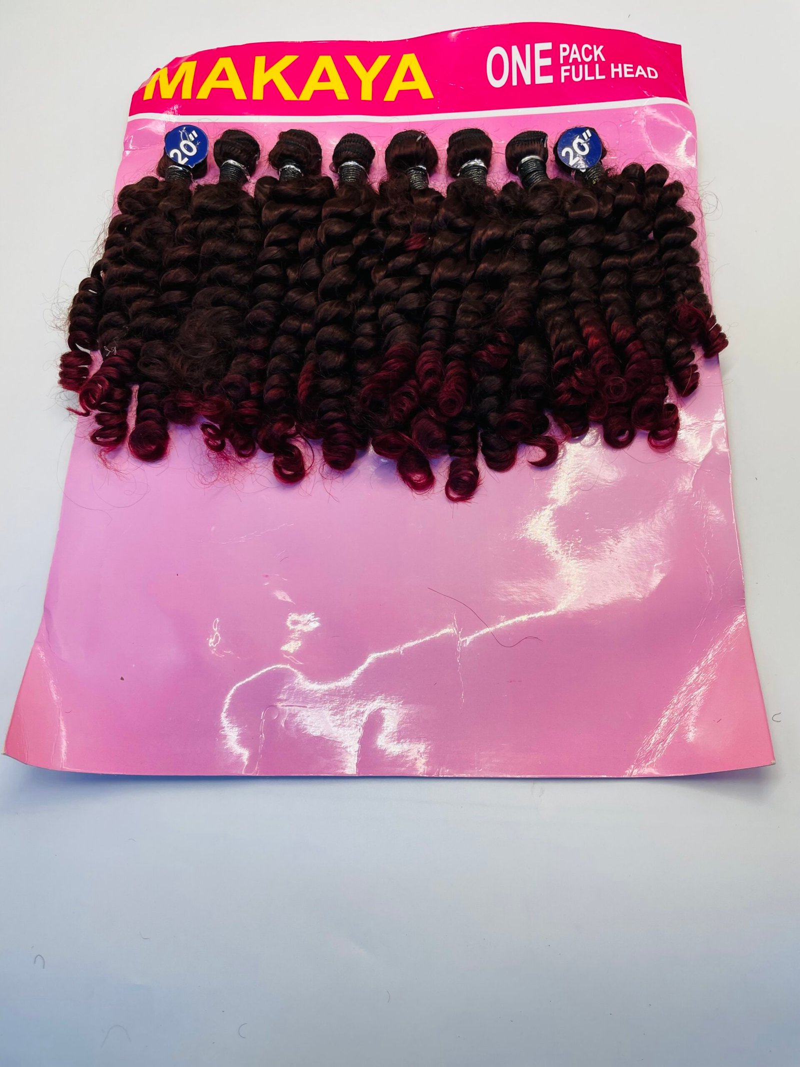 Bundle of tight, burgundy-curled hair extensions in pink packaging labeled 'MAKAYA' and 'ONE PACK FULL HEAD'