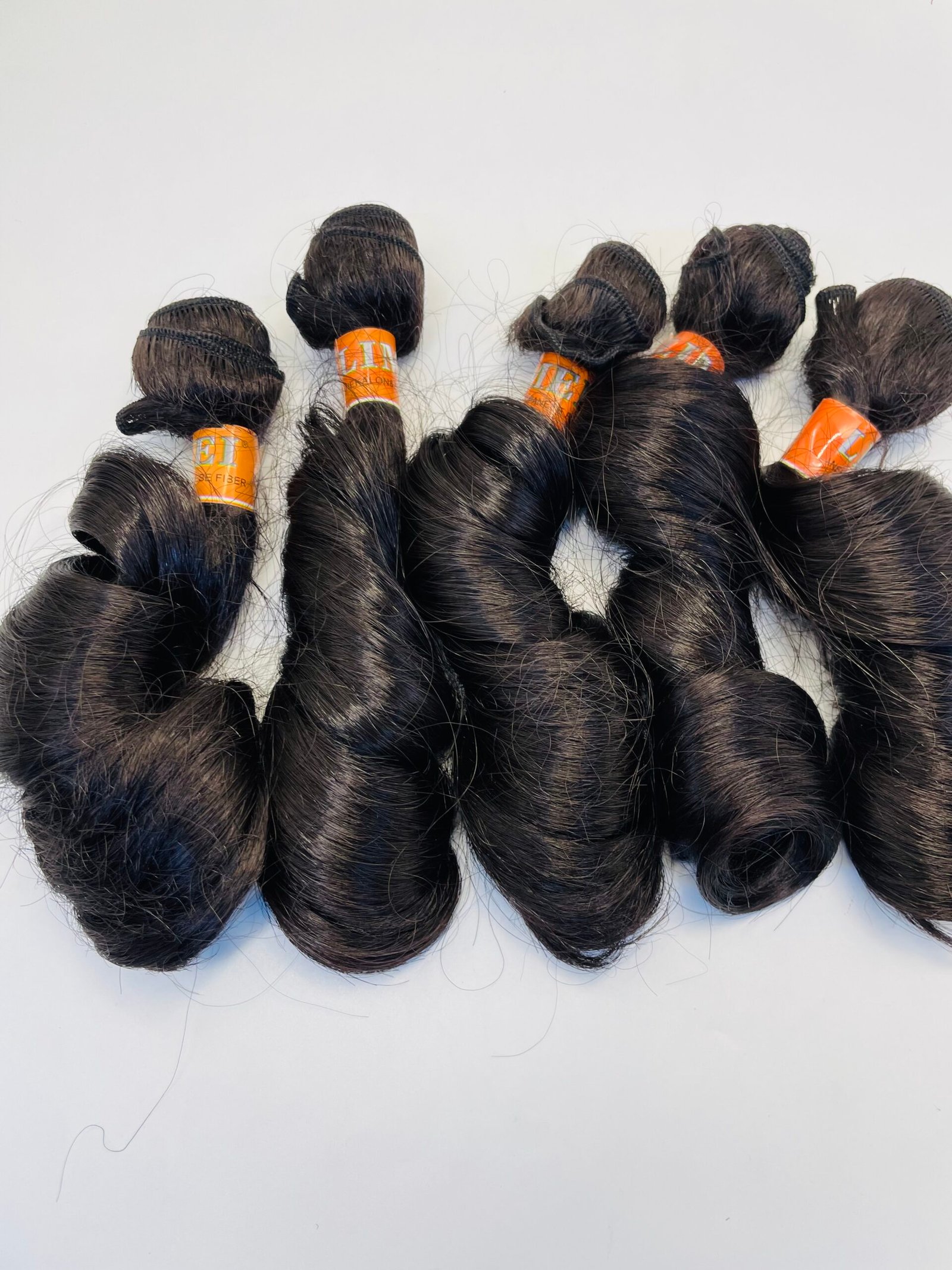 Bundles of dark brown hair extensions tied with orange bands laid on a white surface