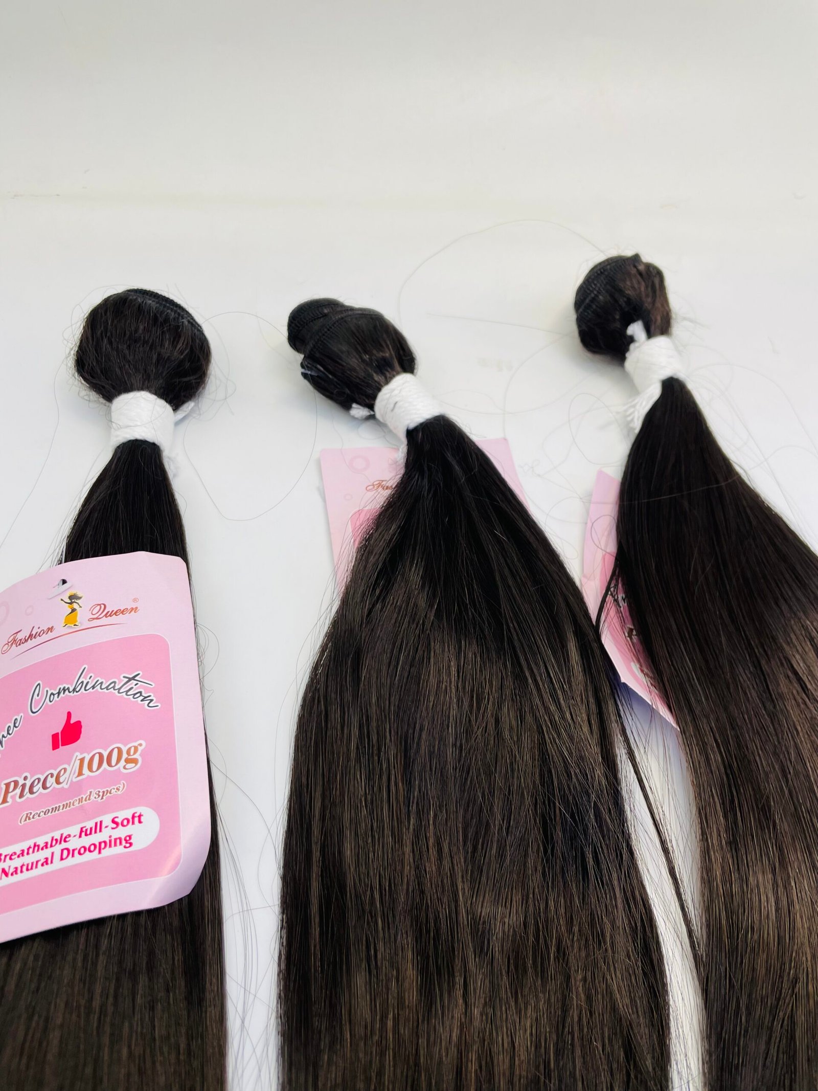 Three bundles of long dark hair tied with white bands, placed on pink product packaging against a light surface (hair extension display).