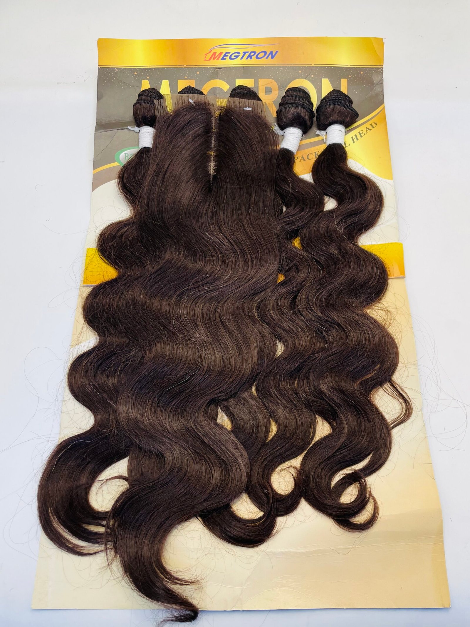 Four bundles of dark brown, wavy hair extensions attached to a yellow display card for sale on a light background.