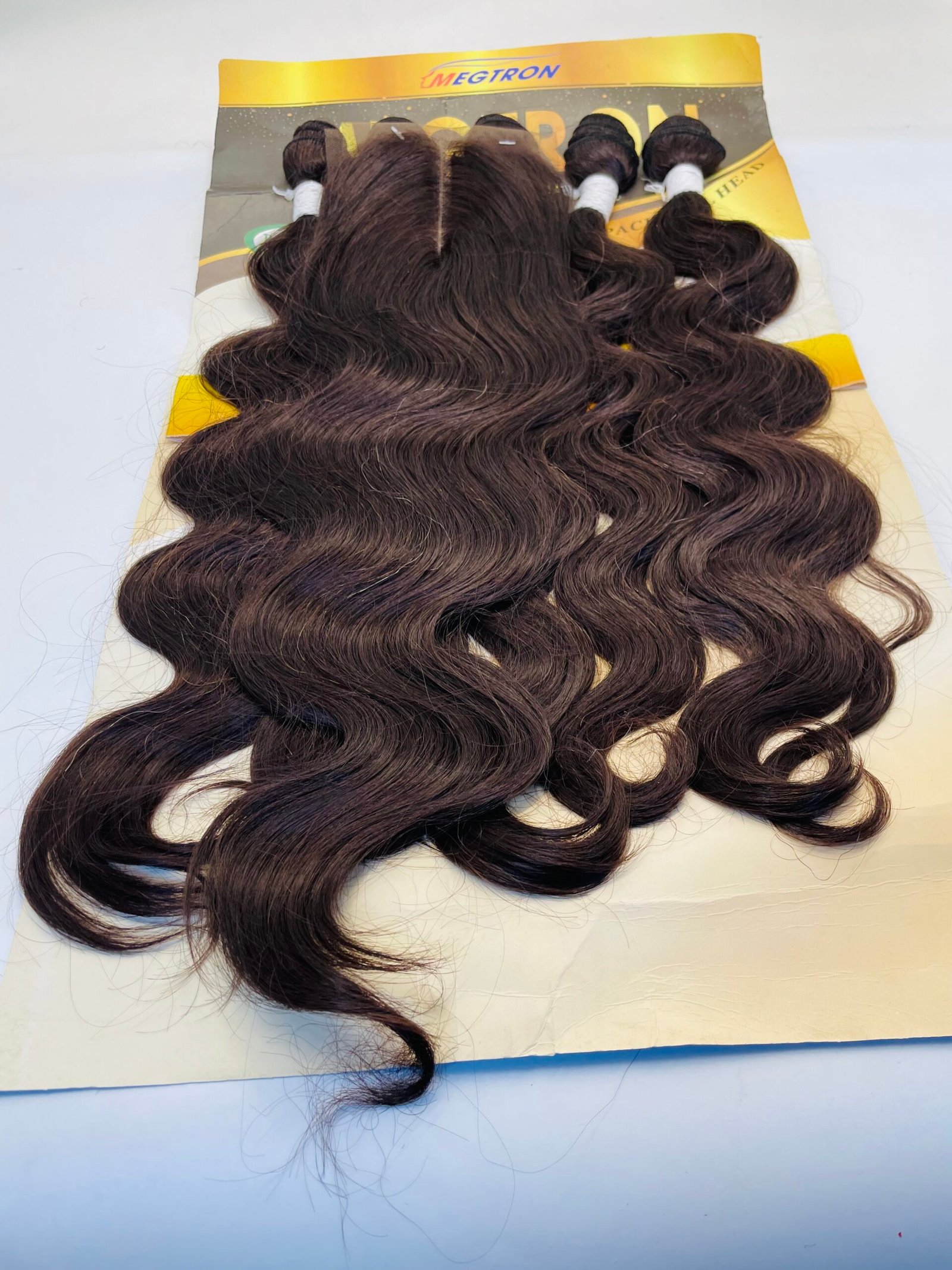 Dark brown wavy hair extensions laid on a cardboard display with bundled sections bound by white bands