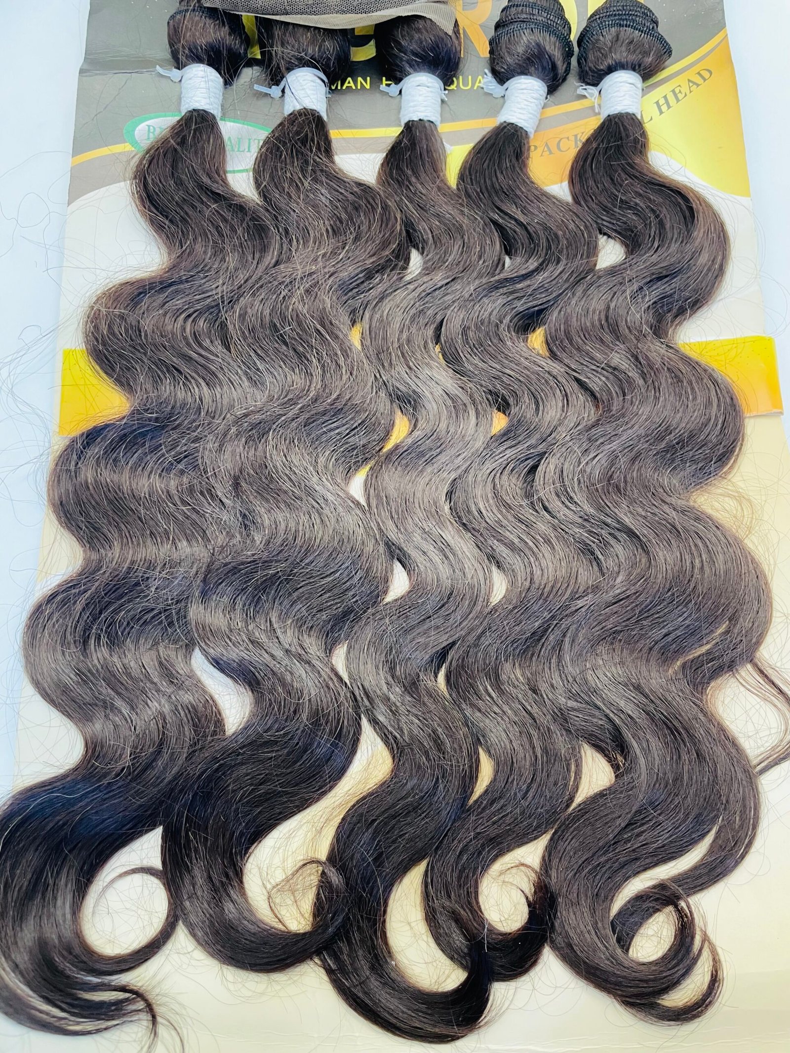 Five dark brown, loose-wavy hair extension bundles tied with white bands on a display card.