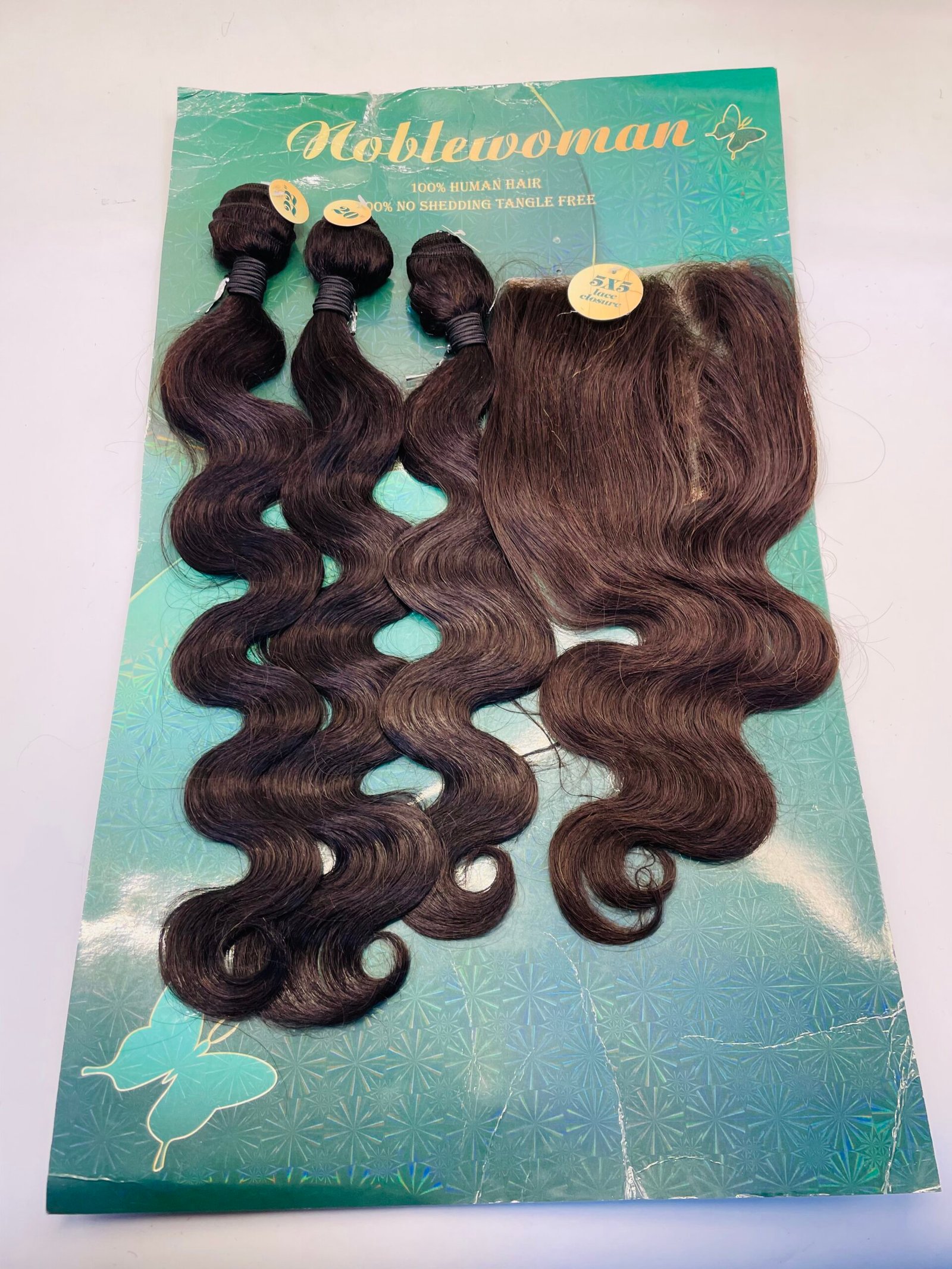 Bundle of dark brown, wavy hair extensions laid on a teal packaging card with a butterfly design