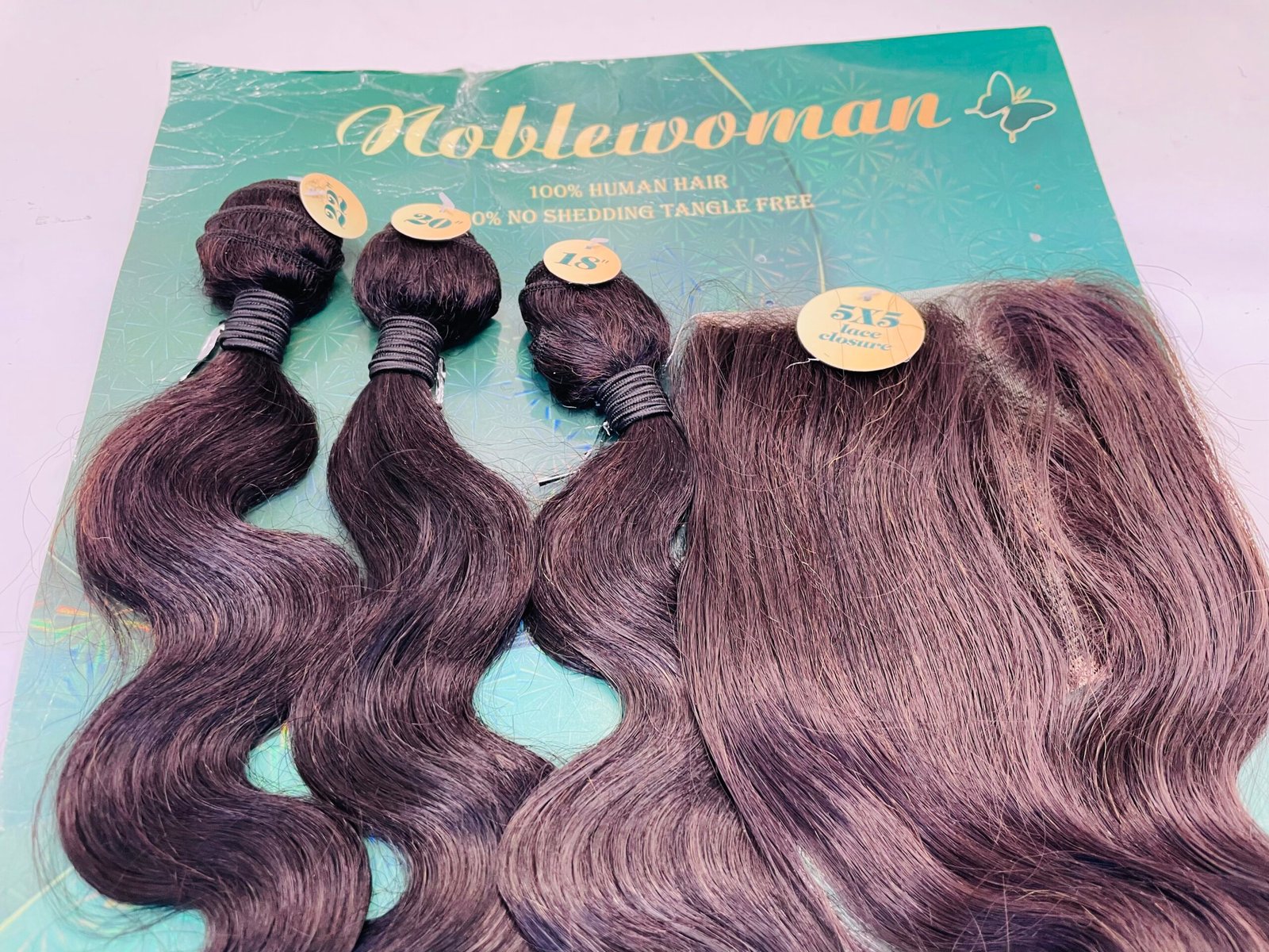 Bundle of dark burgundy hair extensions with yellow size labels laid on a teal Noblewoman display card (product photo).