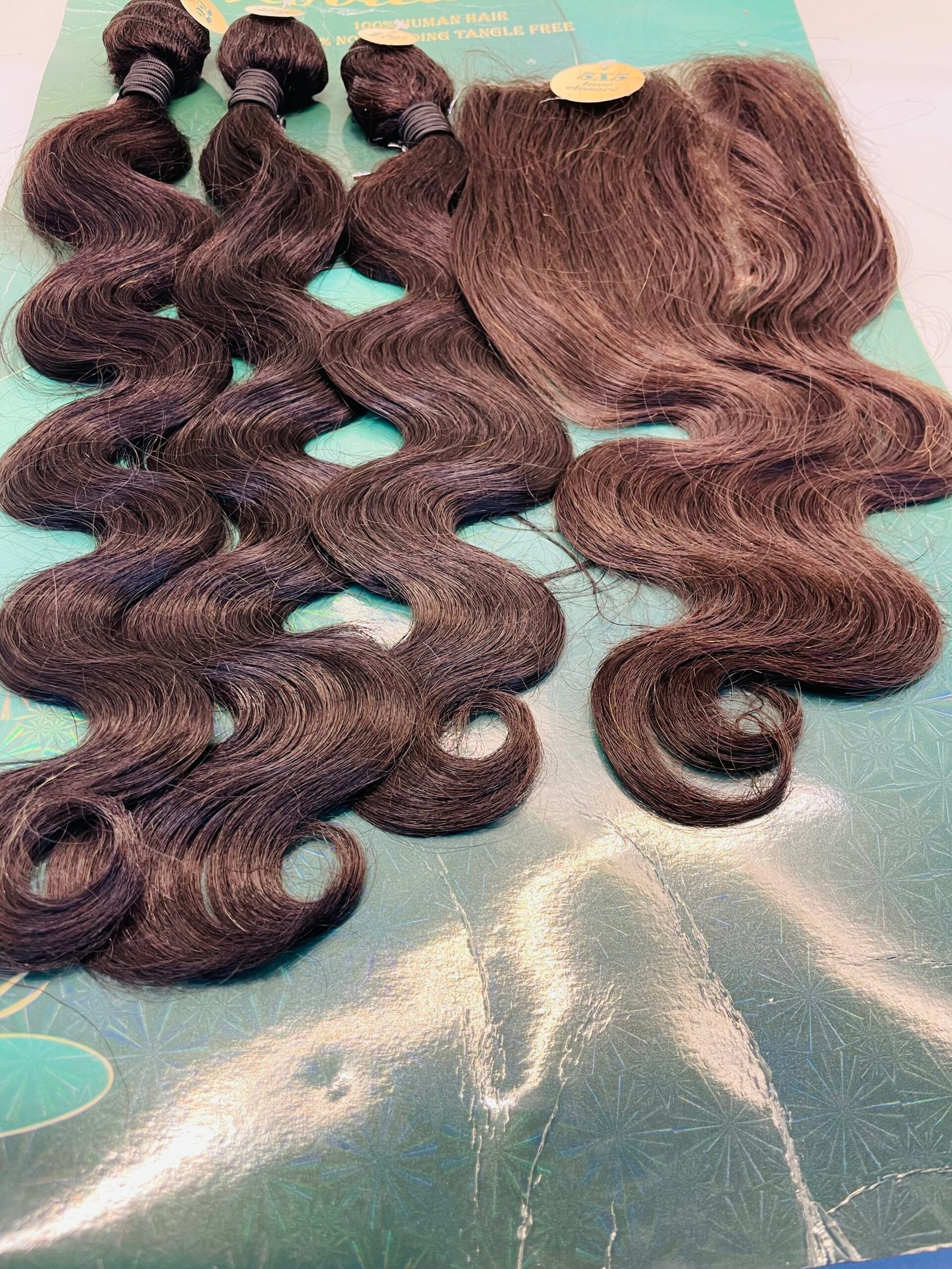 Bundles of wavy brown hair extensions laid on a teal display surface, showing different lengths and textures.