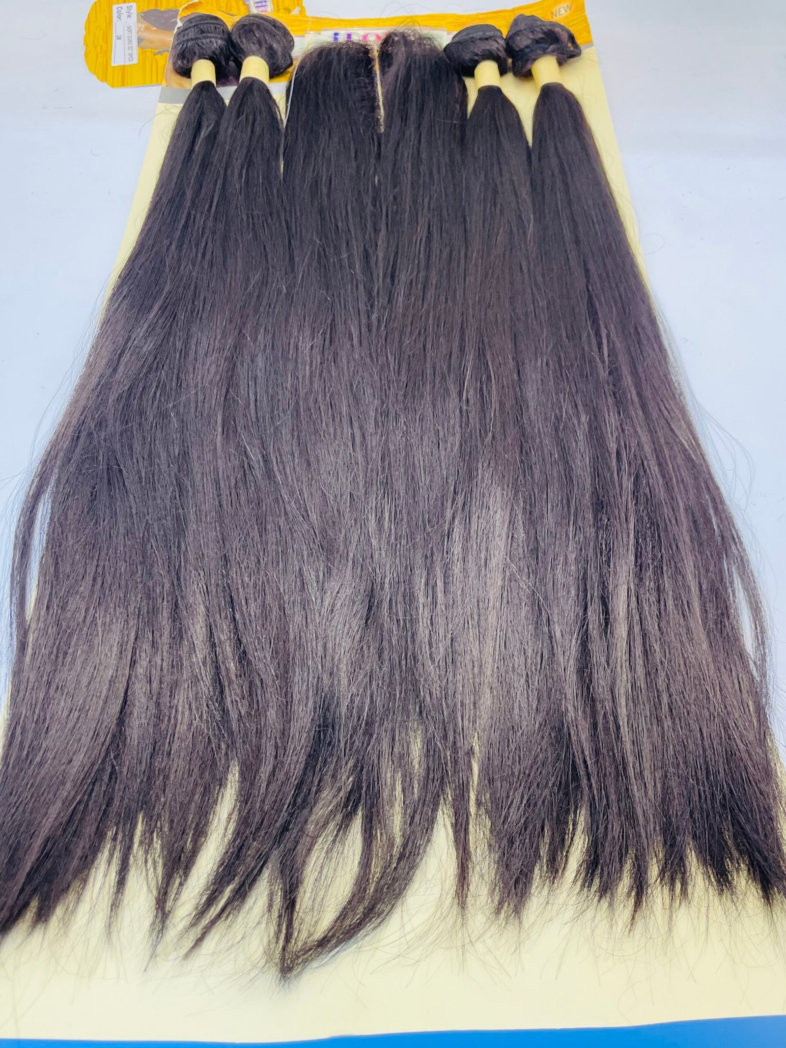 Rows of dark brown hair extensions with beige wefts on a yellow display card at the top edge of the image.