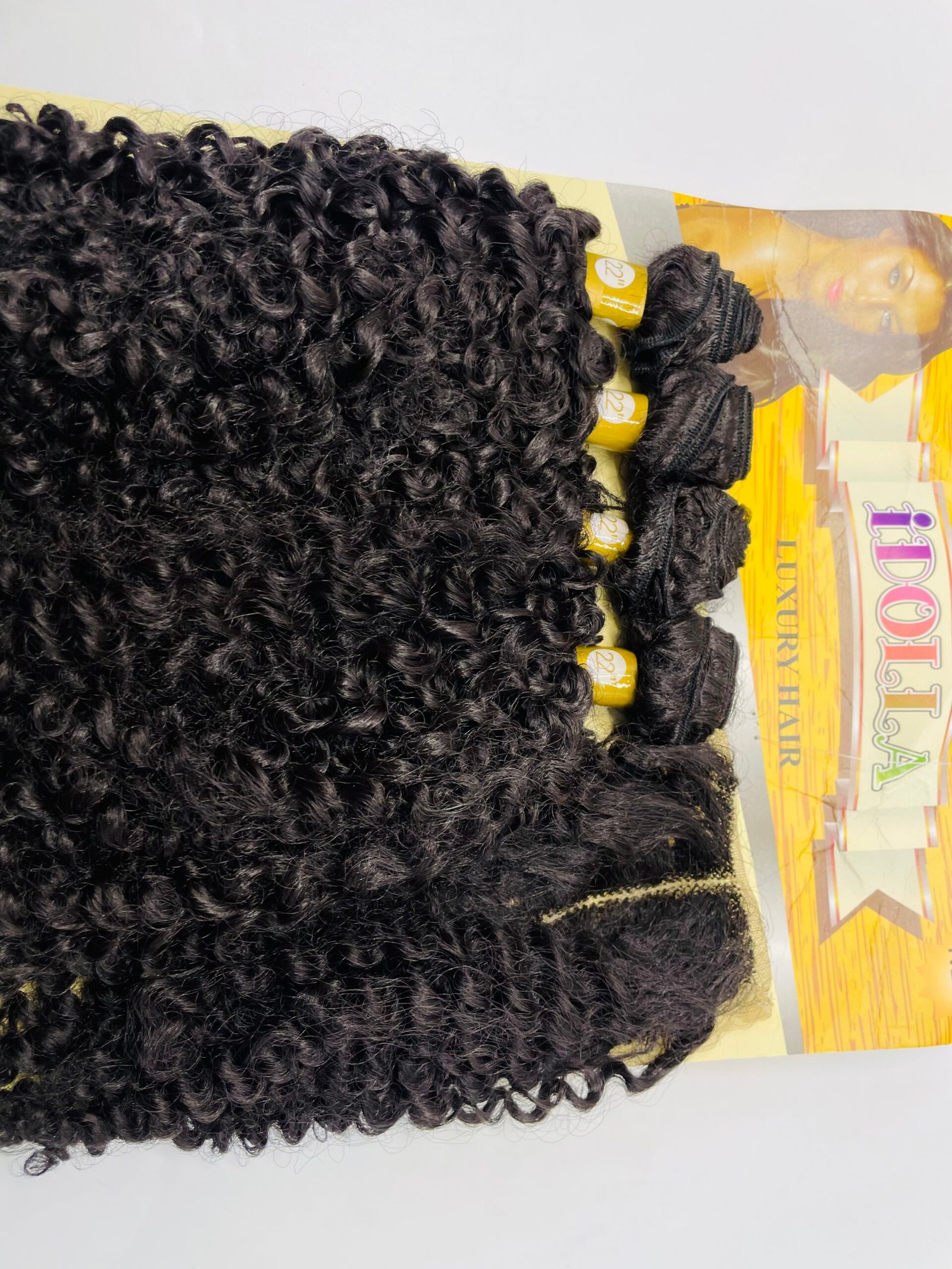 Bundle of tight, black curly hair extensions laid on a magazine page with yellow accents.