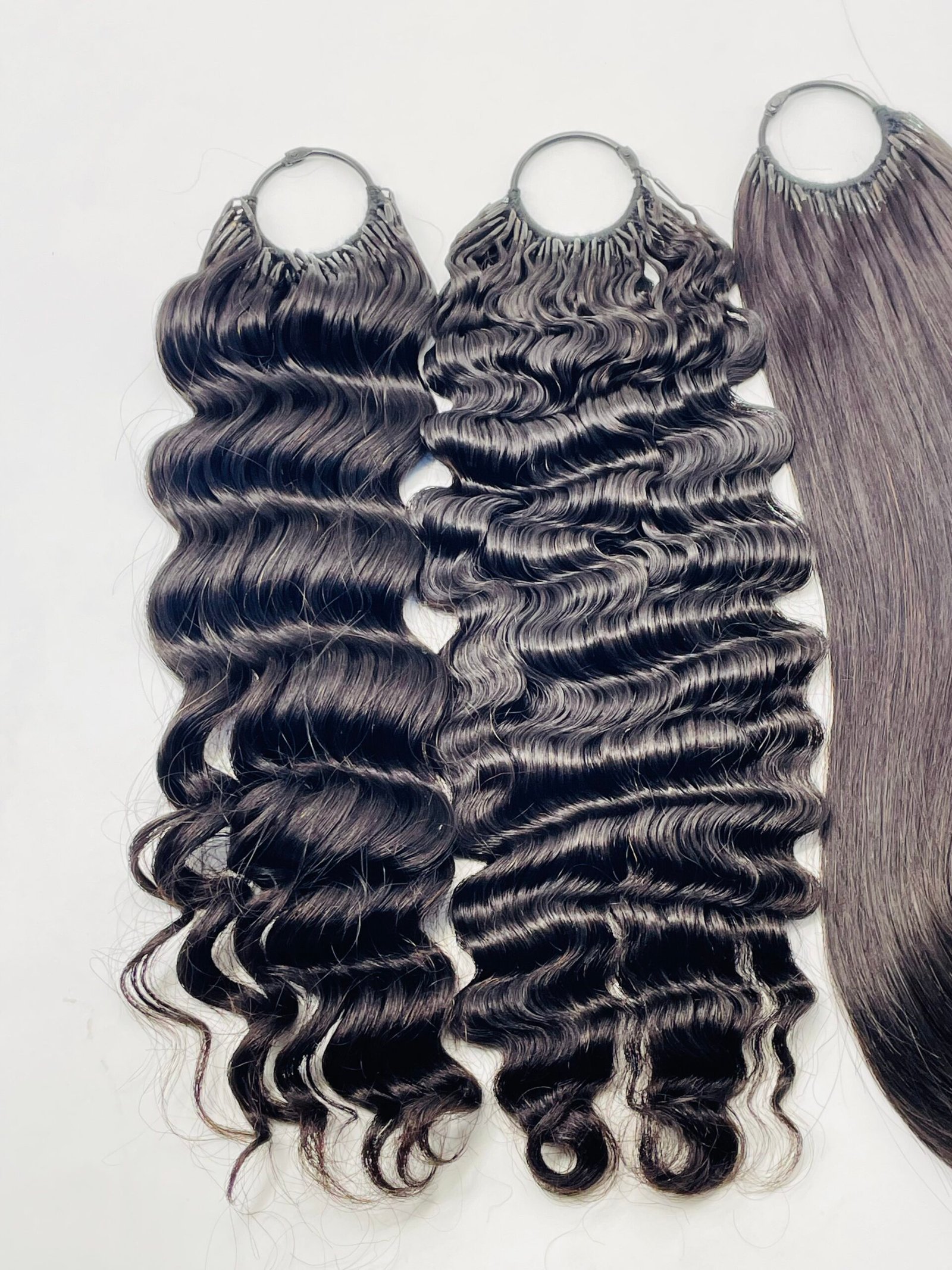 Three bundles of wavy, dark brown/black hair extensions with silver rings at the top, laid on a white background.