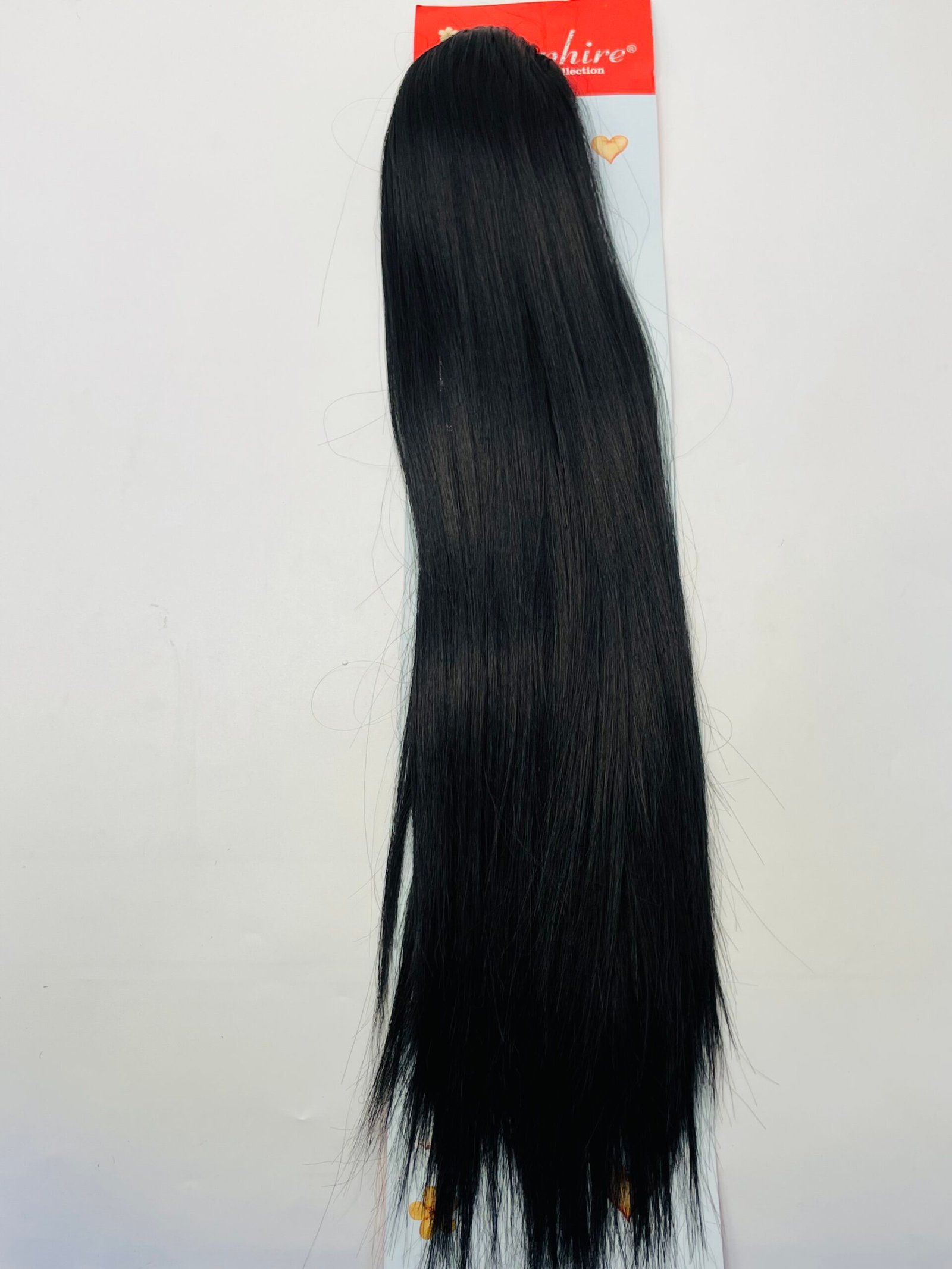 Long, straight black hair extension hanging against a white background with red packaging at the top of the image.