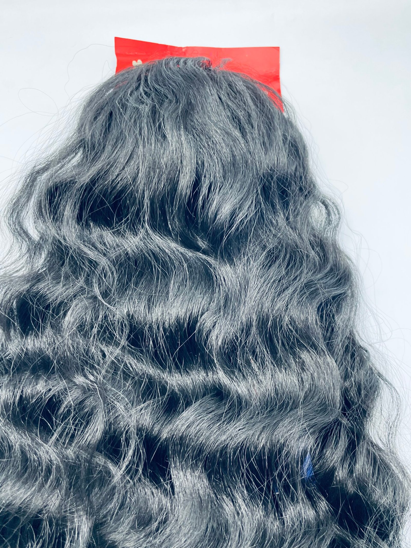Back view of a person with thick gray hair and a small red sticker above the head against a pale background.