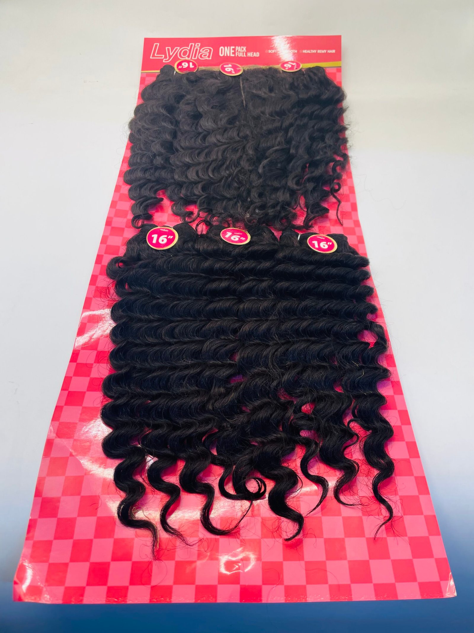 Curly black hair extensions on a pink checkerboard display, 16-inch length labels visible