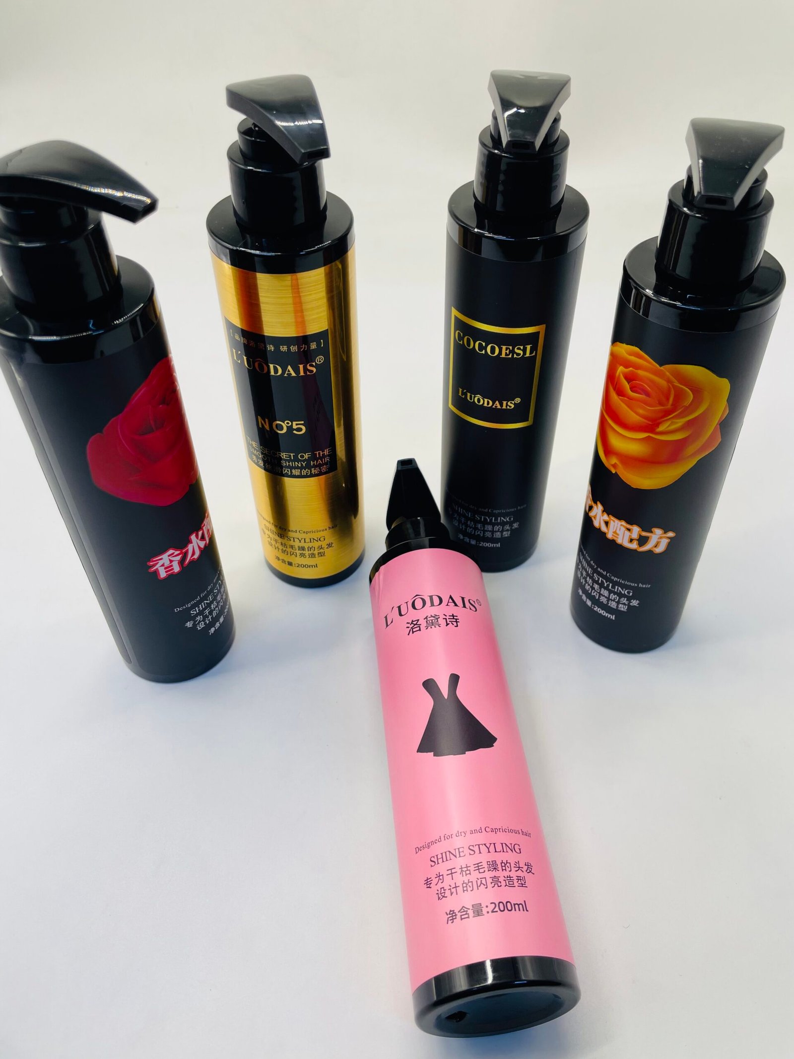 Group of black pump bottles for hair styling, some with rose images and gold labels, standing upright on a white surface.