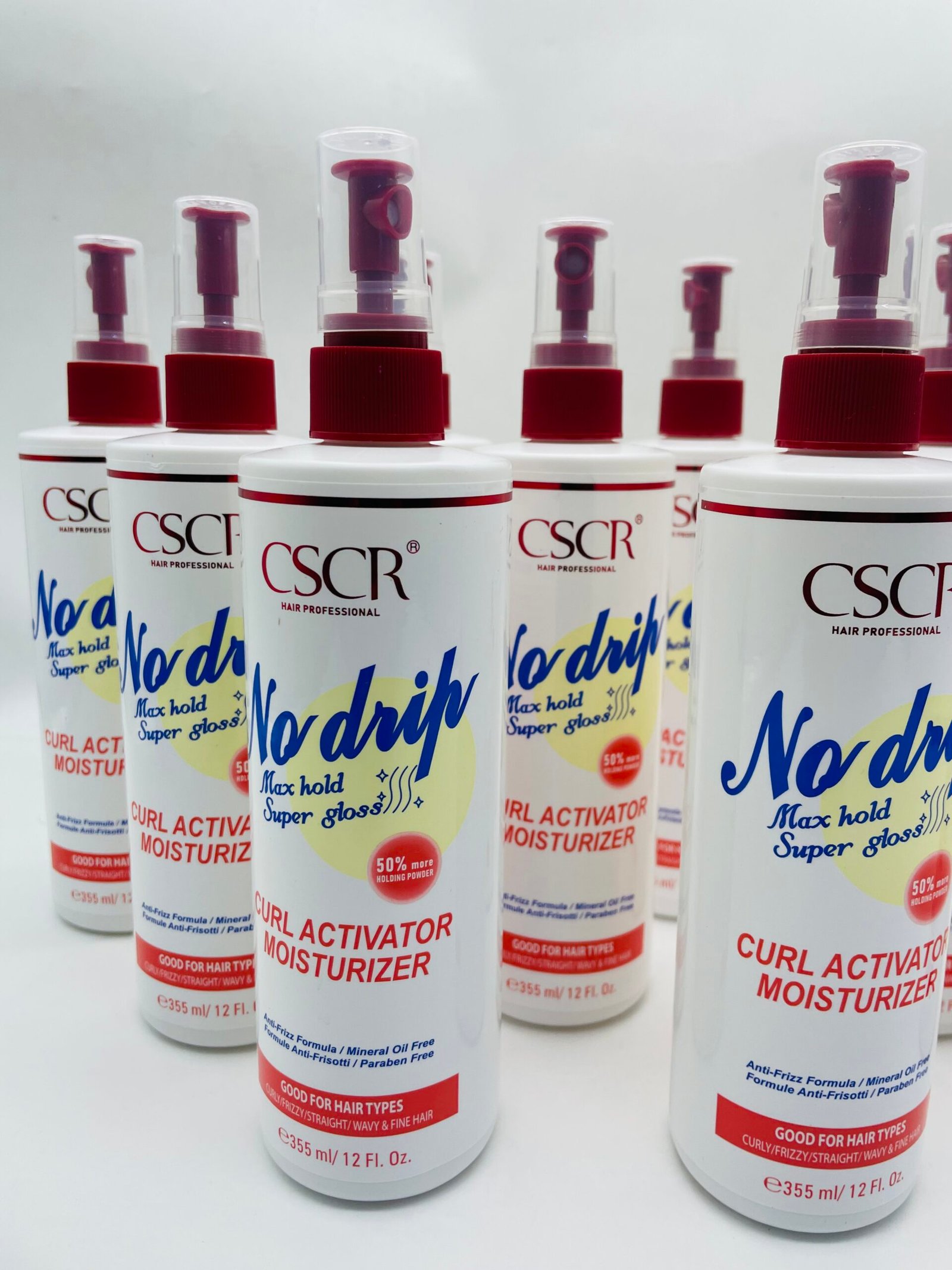 Row of white spray bottles with red caps labeled No-drip Curl Activator Moisturizer, arranged in a line against a white background.