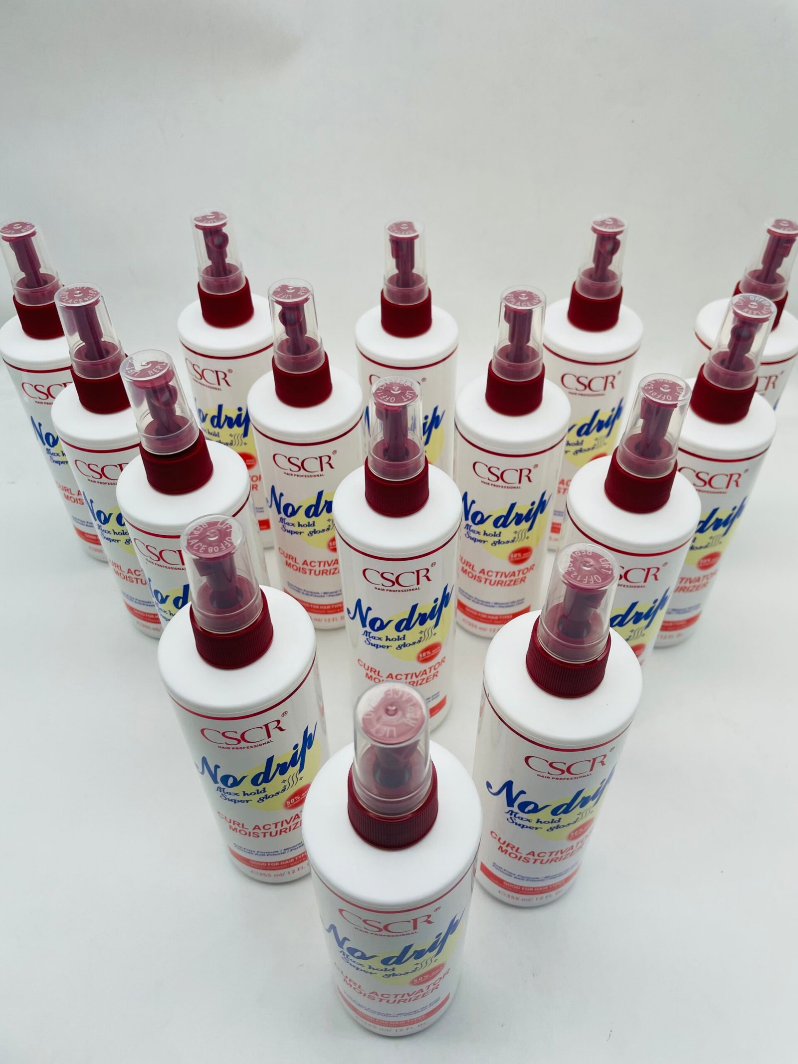 Row of white spray bottles with red caps labeled No Drip curl activator moisturizer on a white surface.