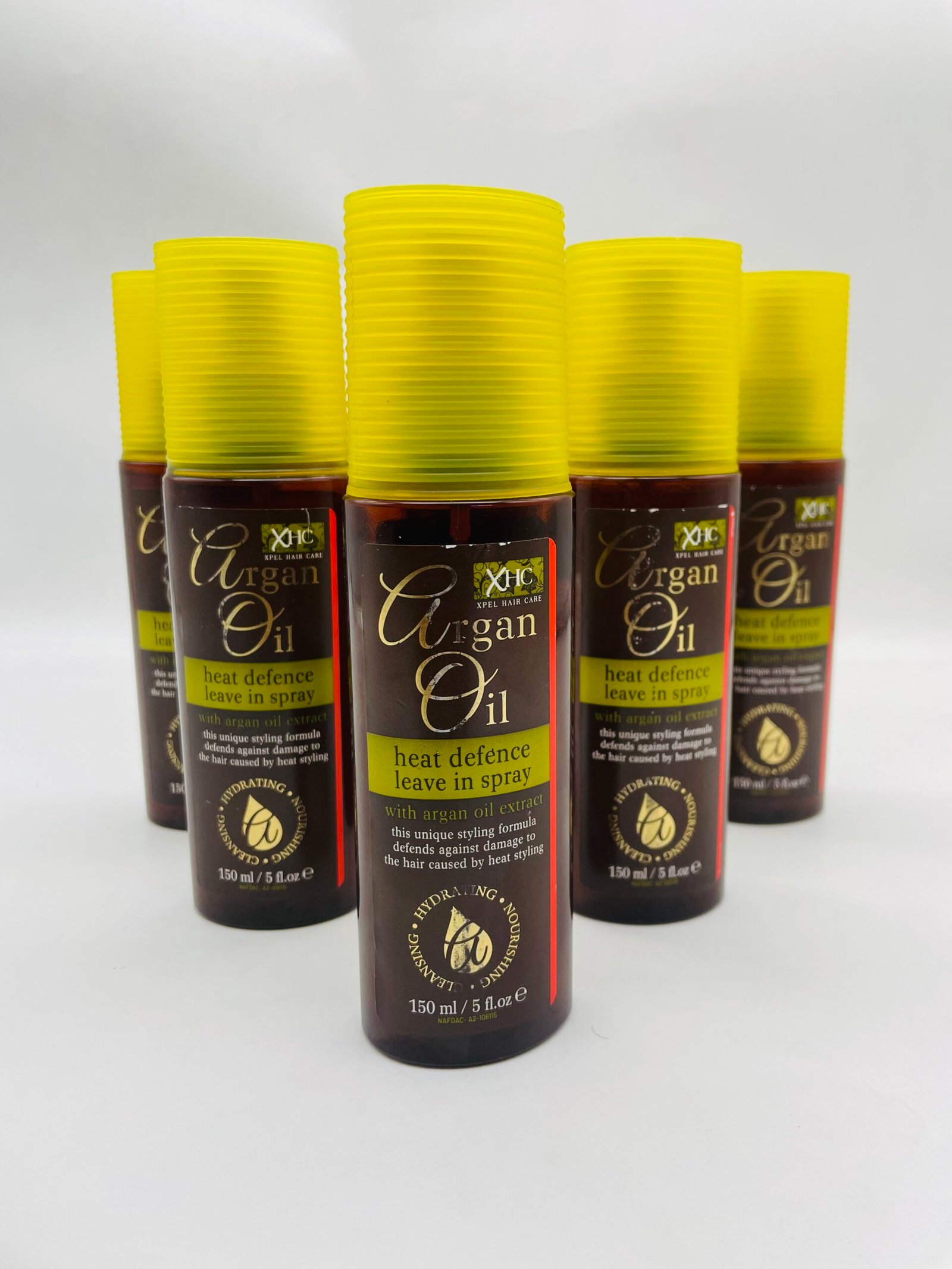 Row of brown Argan Oil hair spray bottles with yellow ribbed caps on a white background, lined up neatly.
