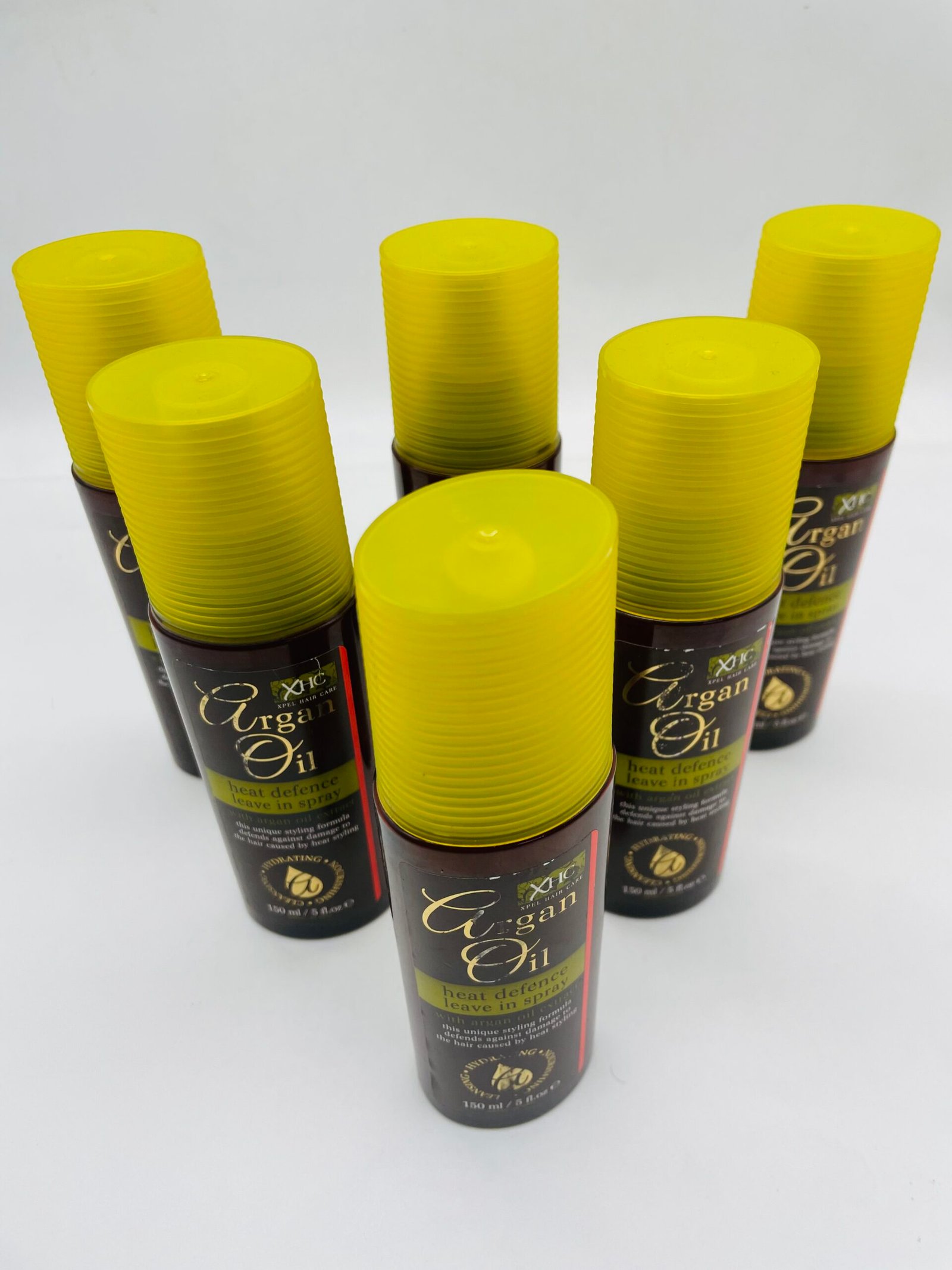 Group of dark brown spray bottles with bright yellow twist-off caps, labeled Argan Oil heat defence leave-in spray.