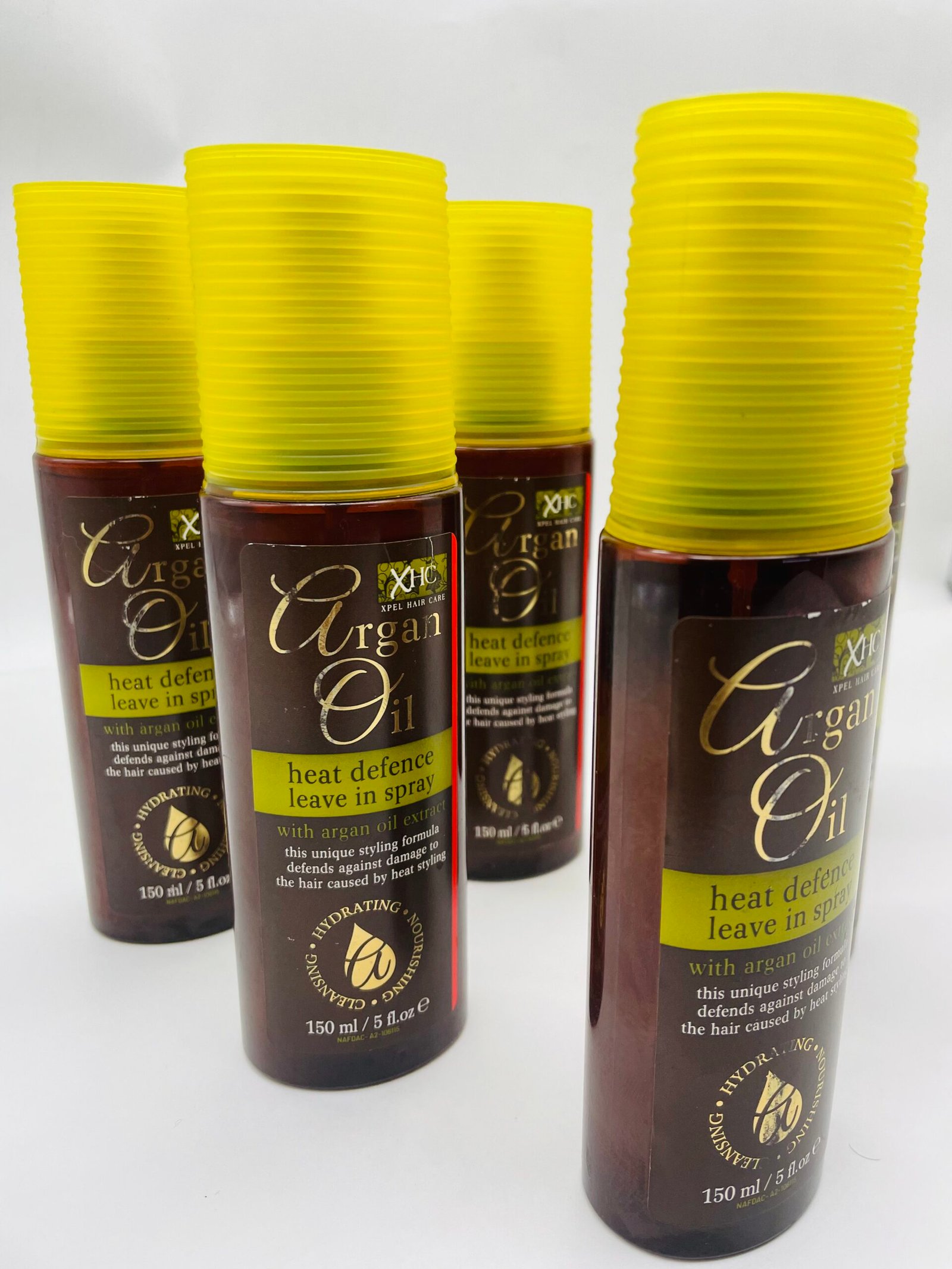 Brown bottles of Argan Oil heat defence spray with bright yellow ribbed caps arranged in a row, product labels visible