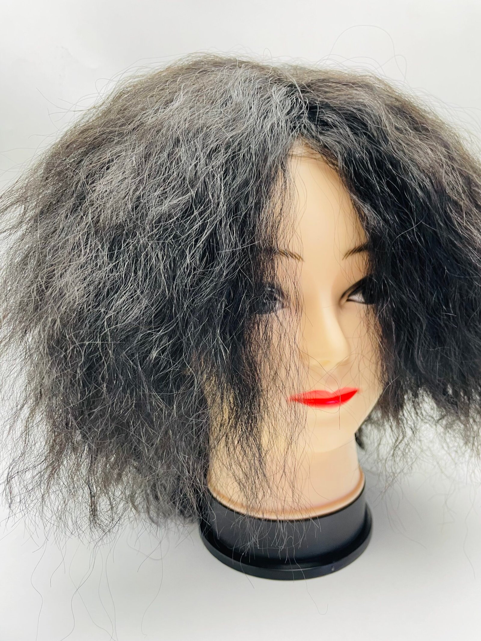 Mannequin head wearing a voluminous black-and-gray curly wig with red lips.