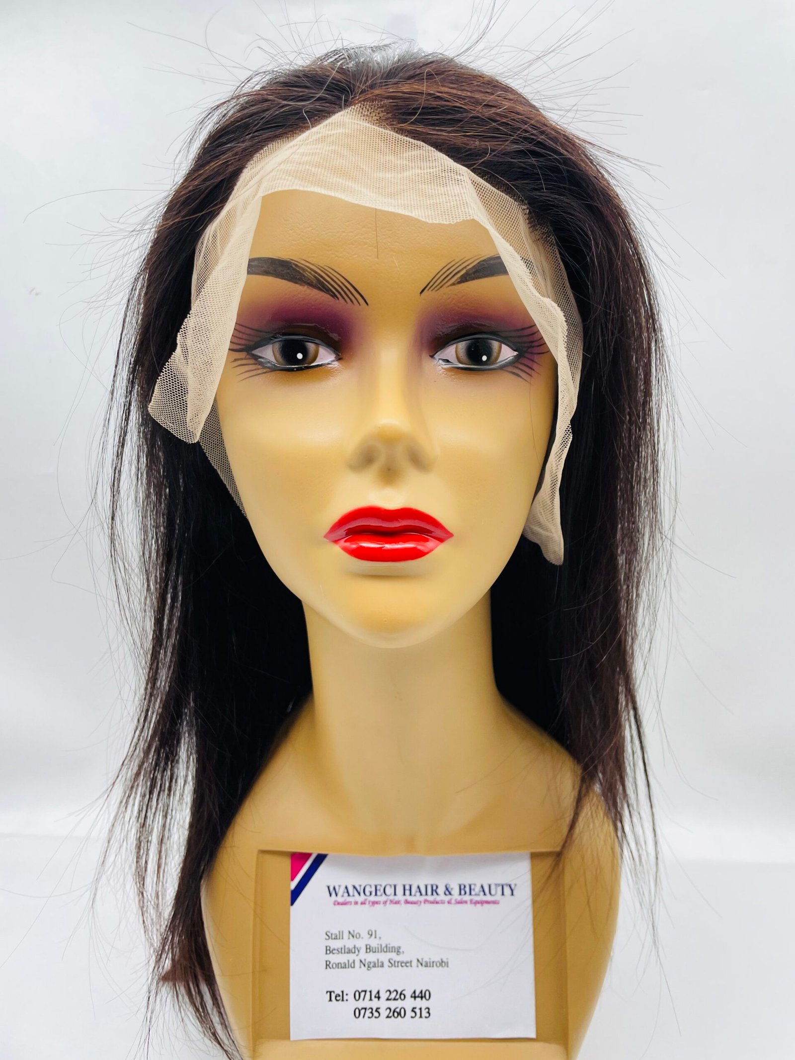 Mannequin head with dark wig and beige bandage-like wrap around the forehead, displaying hair product setup.